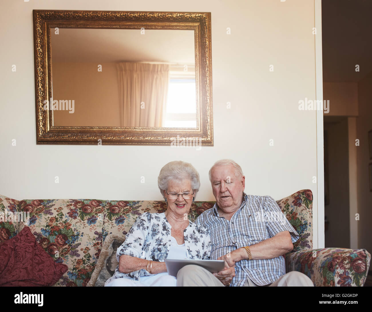 Portrait of happy old couple sitting together at home on sofa and using digital tablet. Elderly man and woman using touchscreen Stock Photo