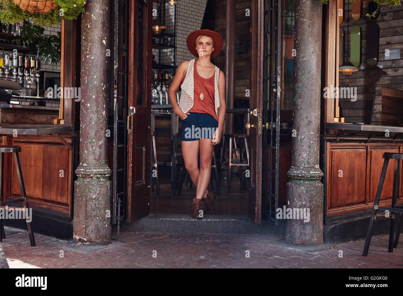 Full length shot of young urban woman leaving a cafe. Trendy young woman walking out of a coffee shop. Stock Photo