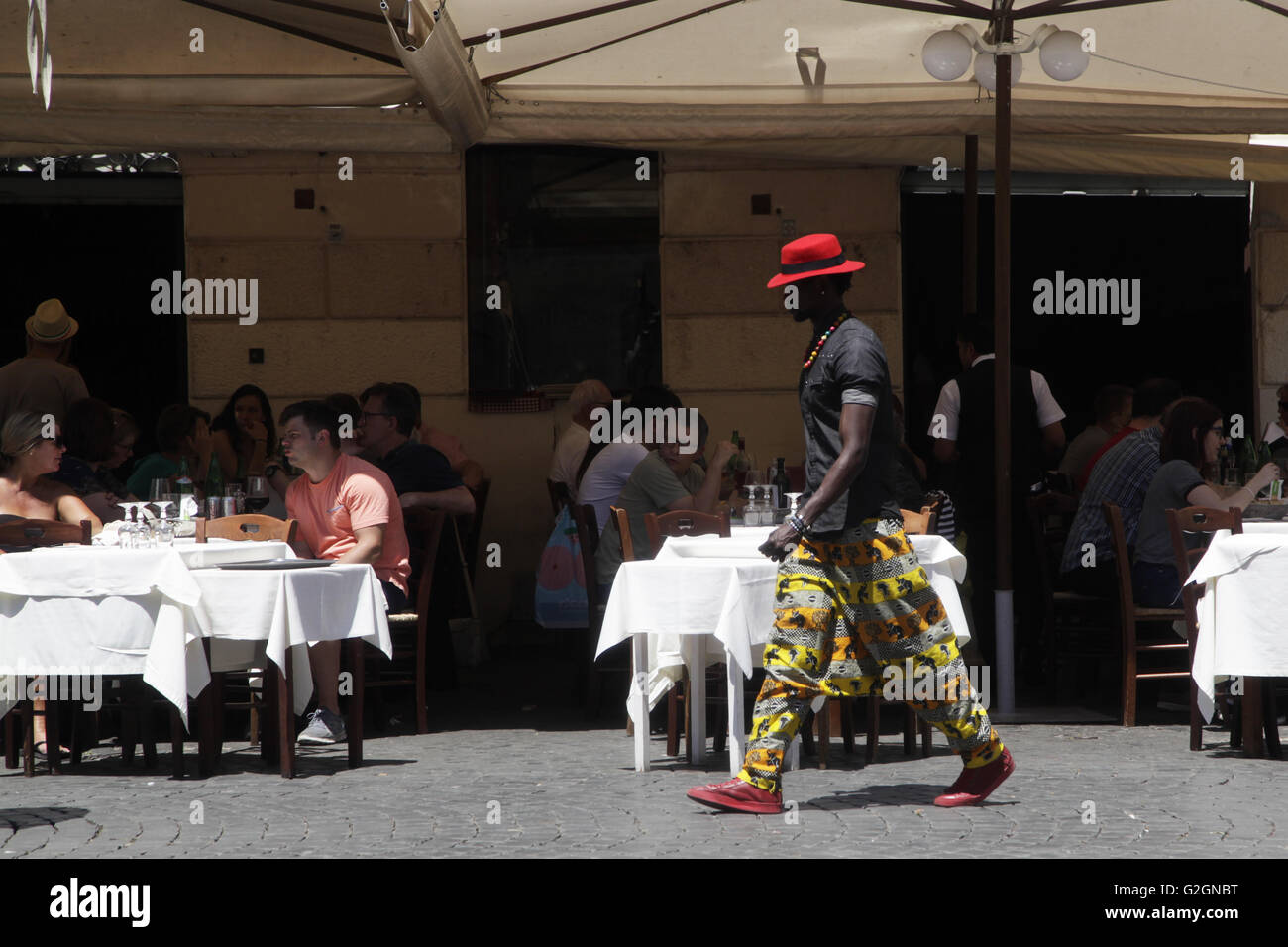 Young black man in colorful dressed walk past at at traditional italian restaurant in Trastevere Rome, Italy Stock Photo