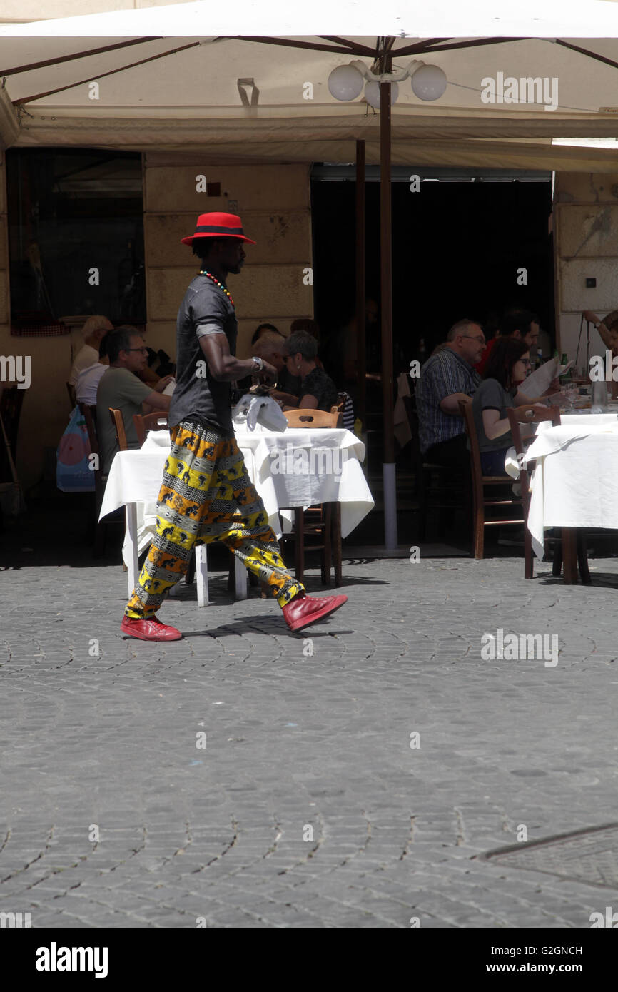 Young black man in colorful dressed walk past at at traditional italian restaurant in Trastevere Rome, Italy Stock Photo