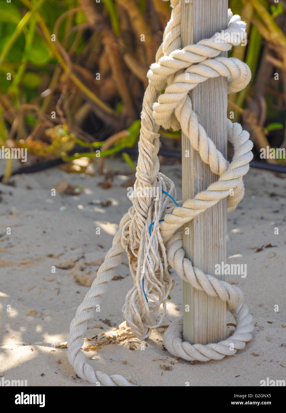 old rope wrapped around a pole that is surrounded by sand, beach Stock Photo