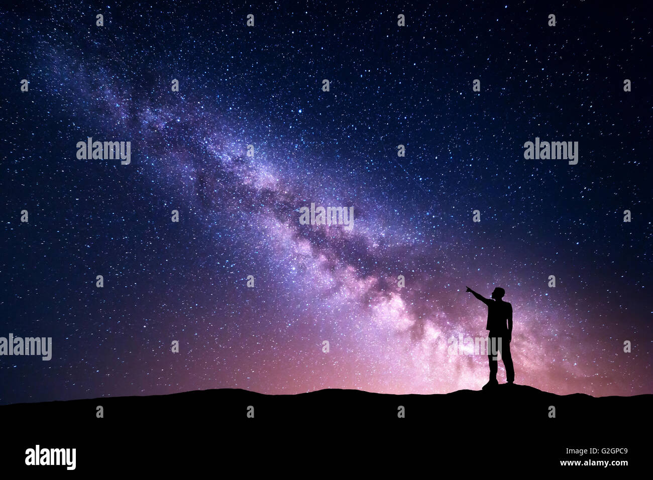 Milky Way with silhouette of a standing young man pointing finger in night starry sky on the mountain. Night landscape Stock Photo