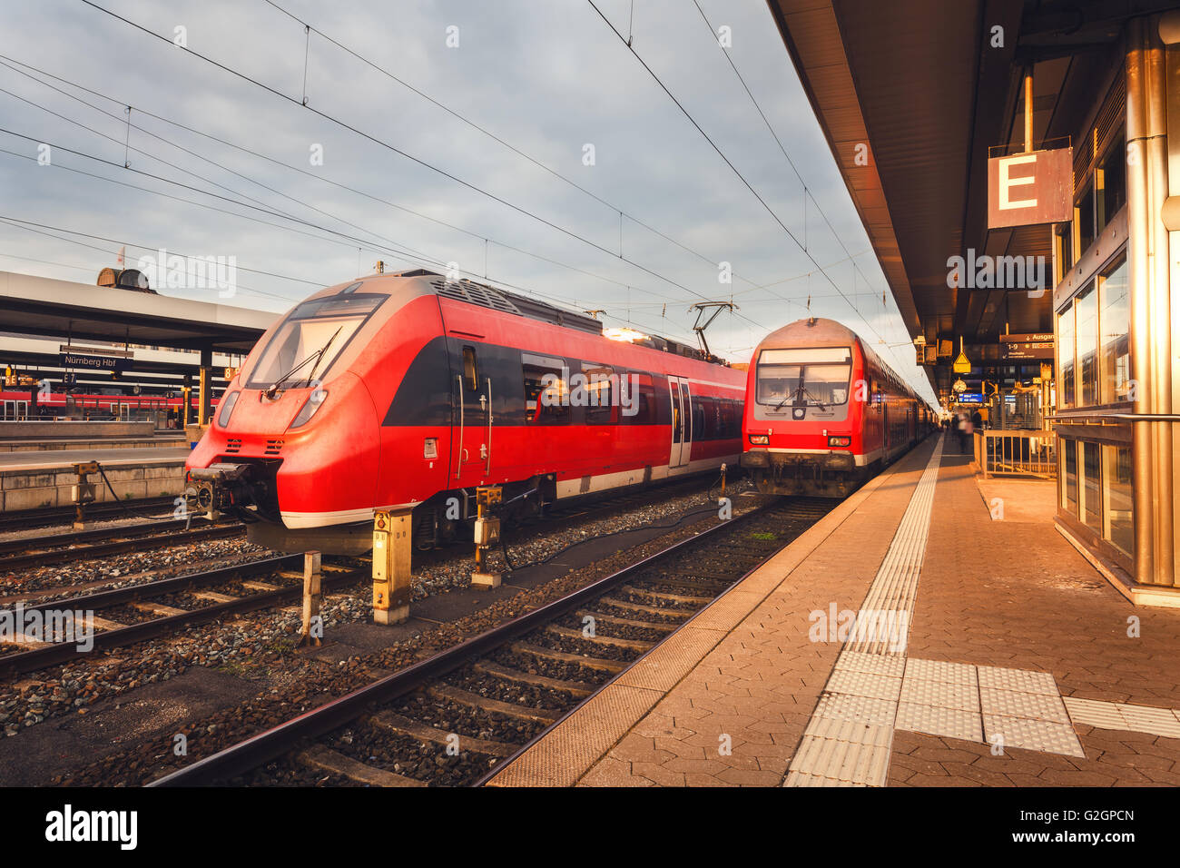 Beautiful railway station with modern red commuter train at colorful sunset in Nuremberg, Germany. Railroad with vintage toning Stock Photo