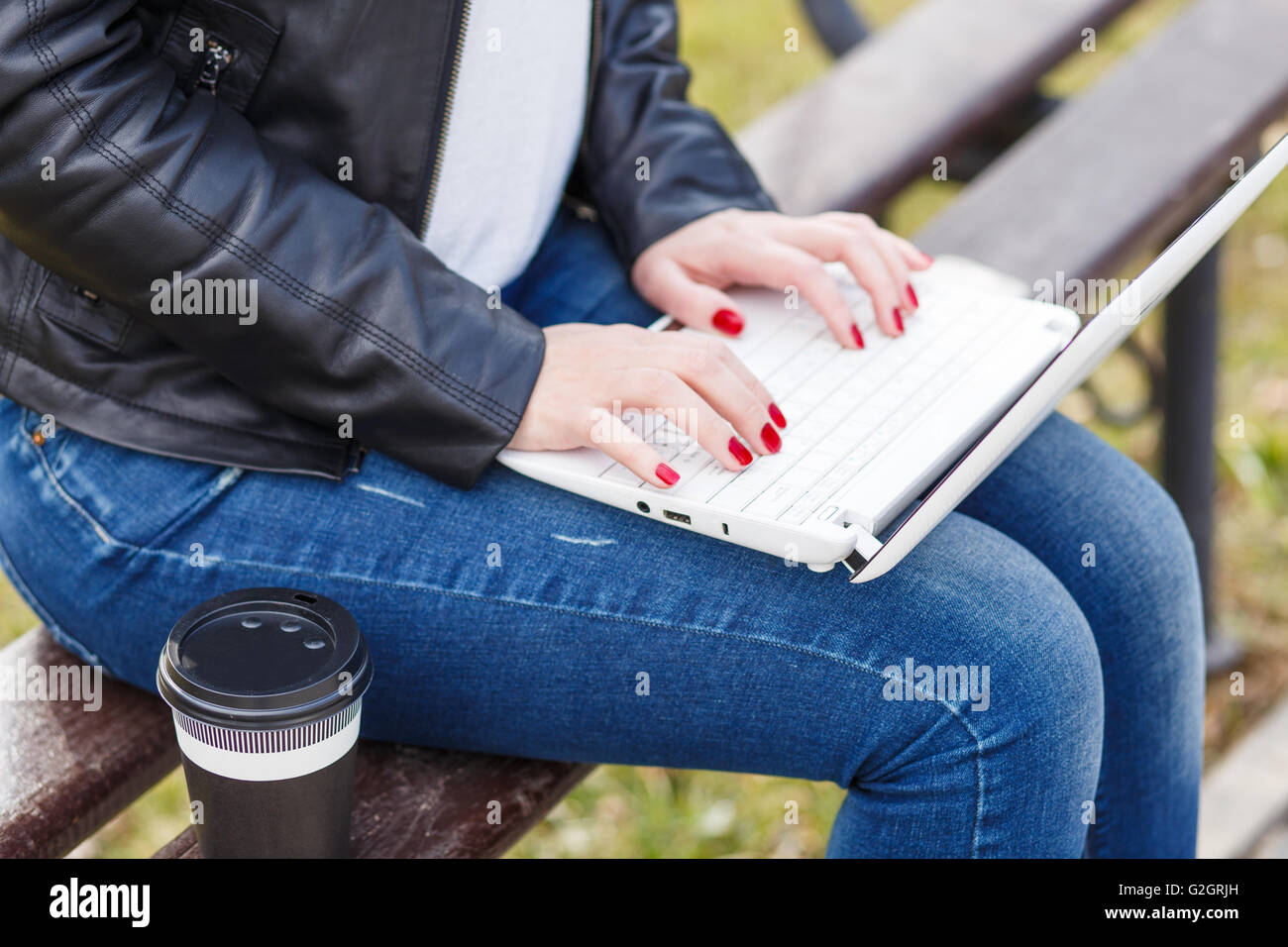 Young woman has coffee break sitting with laptop on bench in park Stock Photo