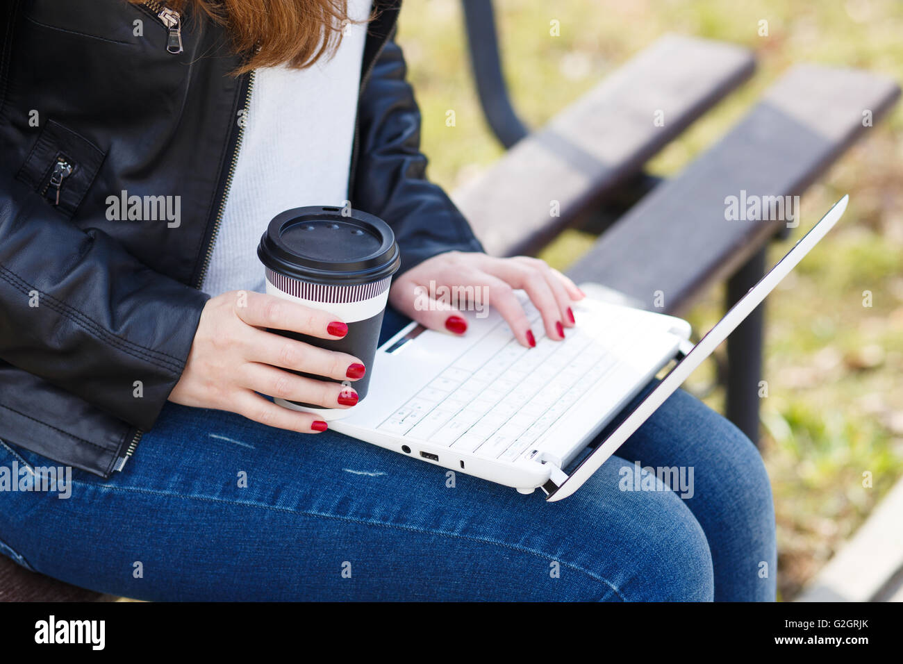 Young woman has coffee break sitting with laptop on bench in park Stock Photo