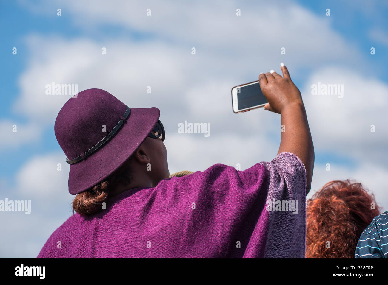 A spectator wearing a hat at the Lowveld Airshow taking a video with her cell phone Stock Photo