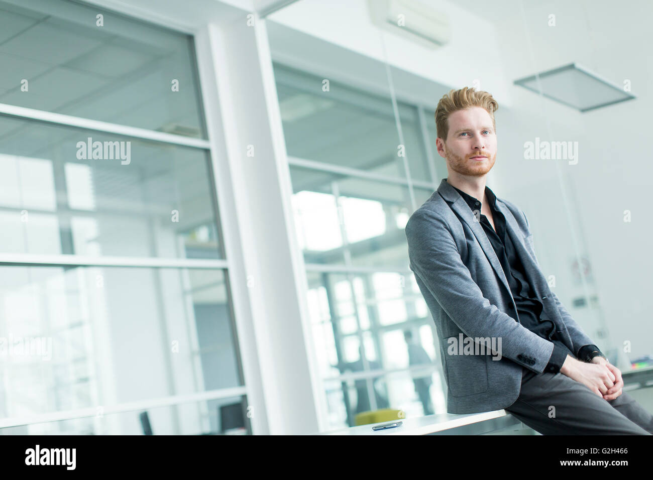 Young businessman sitting on the desk in the office Stock Photo - Alamy