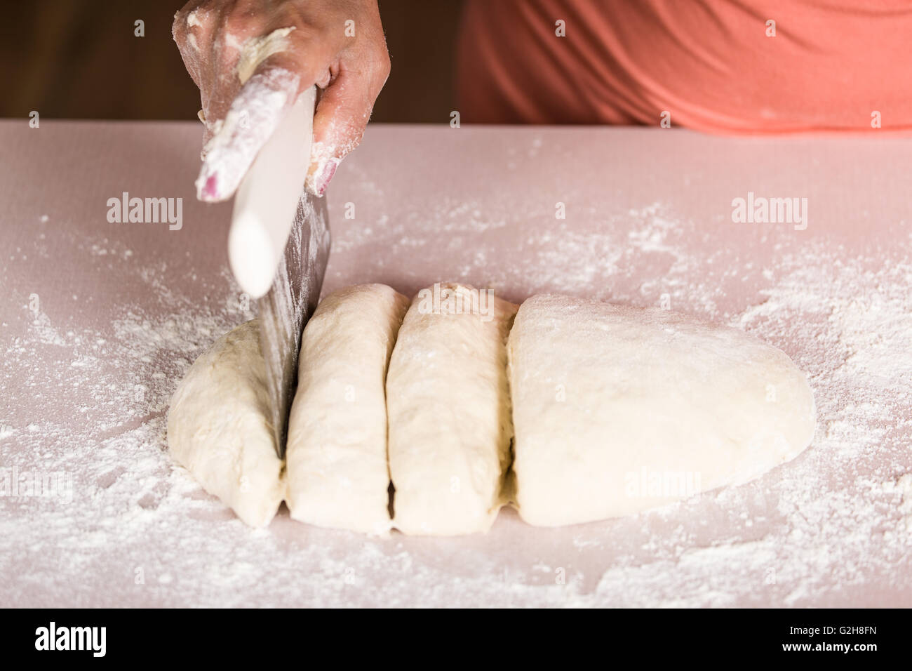 Woman using a dough cutter to divide the naan bread dough into six equal portions which are flattened and baked.  Bakers and pas Stock Photo