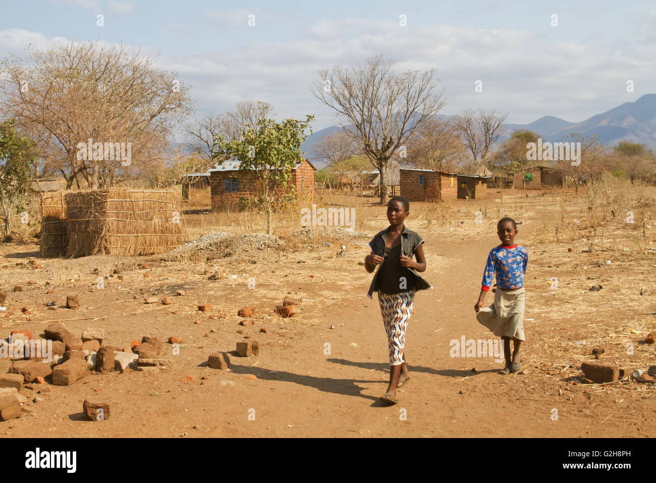 Girls walking by small brick homes in the Chiawa Cultural Village on the Zambezi River in Zambia, Africa Stock Photo