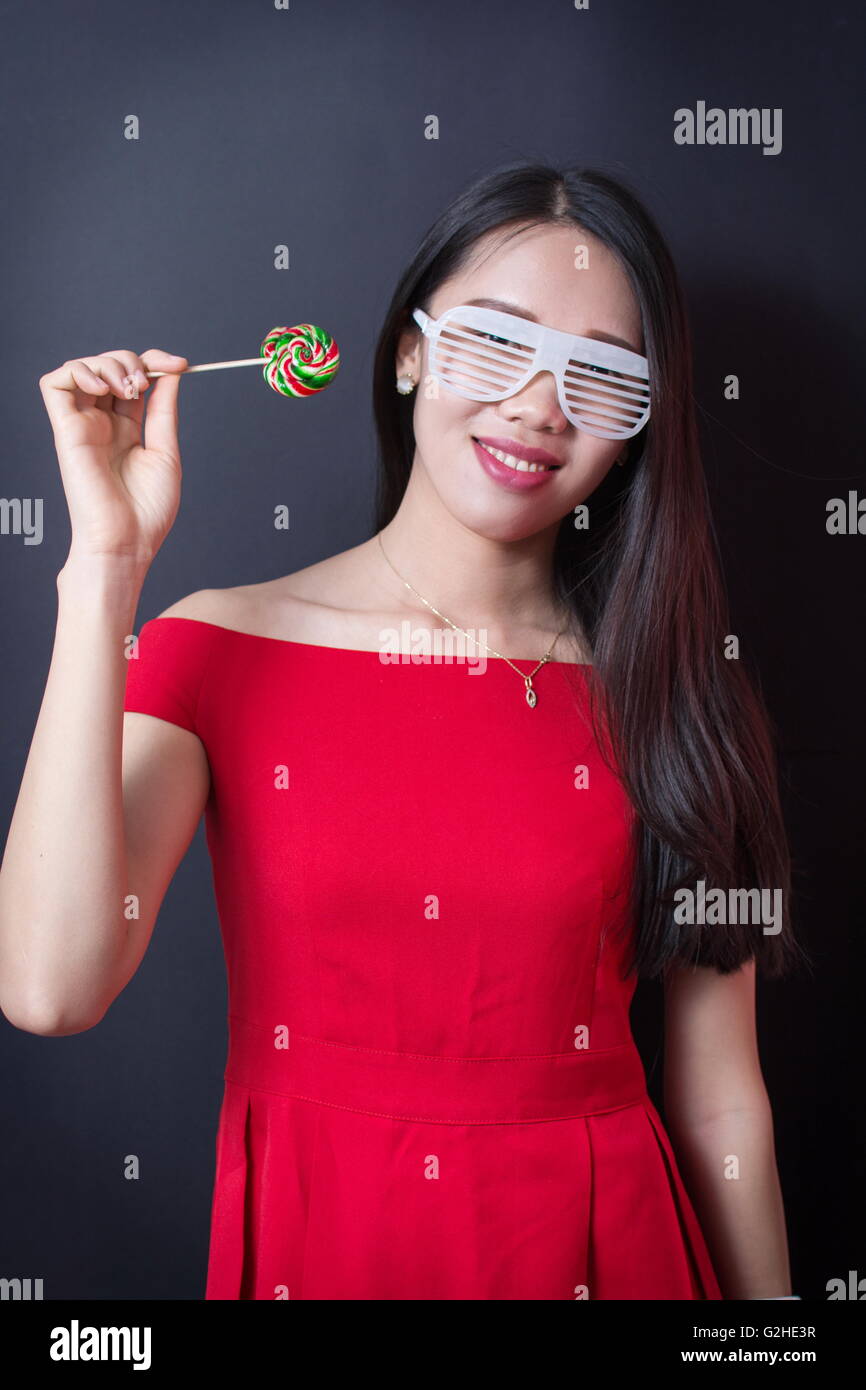 Beautiful woman holding a lollipop while wearing red dress Stock Photo