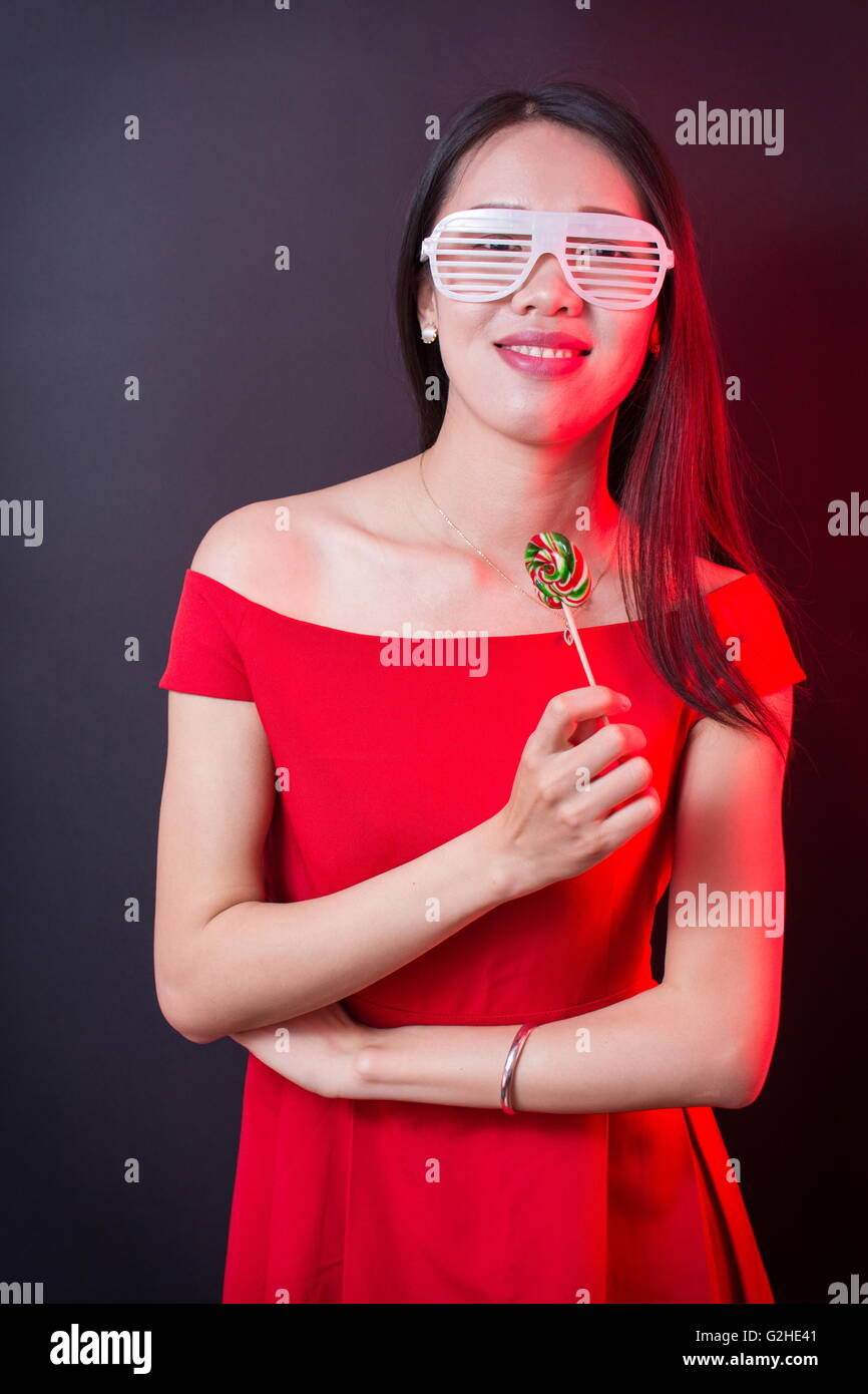 Beautiful woman holding a lollipop while wearing red dress Stock Photo