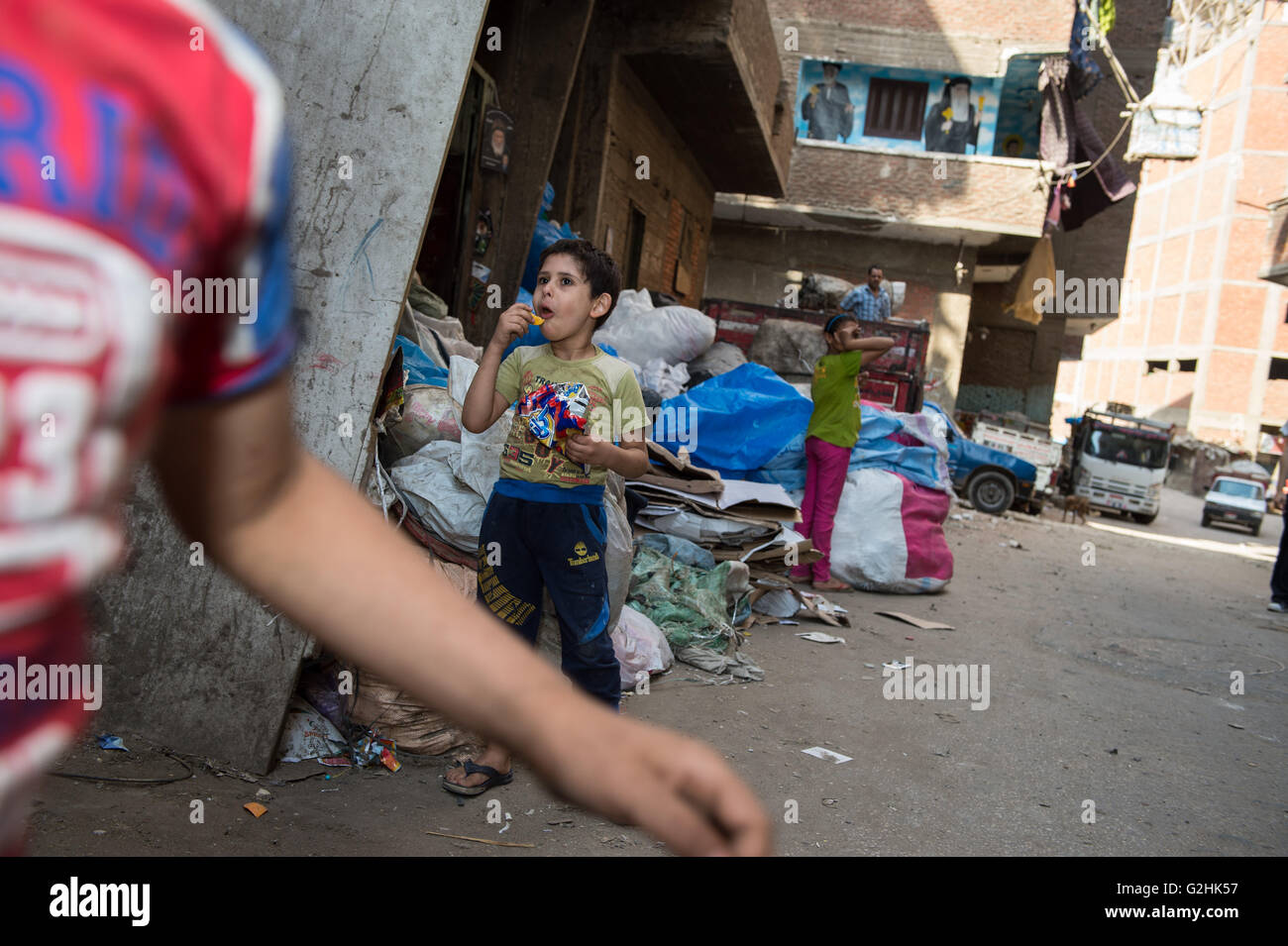 Cairo, Egypt. 27th May, 2016. A boy eats snacks in an alley at the Al-Mokattam City, also known as the 'Garbage City', in Cairo, capital of Egypt, on May 27, 2016. Living on the outskirts of Cairo, the Zabalen, which literally means 'garbage people', is a community that has been collecting and recycling Cairo's waste for a long time. They collected and sorted the waste for a living at Al-Mokattam City. The children here live and play among the garbage and lots of them have dropped out of school to help their family's garbage business. © Meng Tao/Xinhua/Alamy Live News Stock Photo