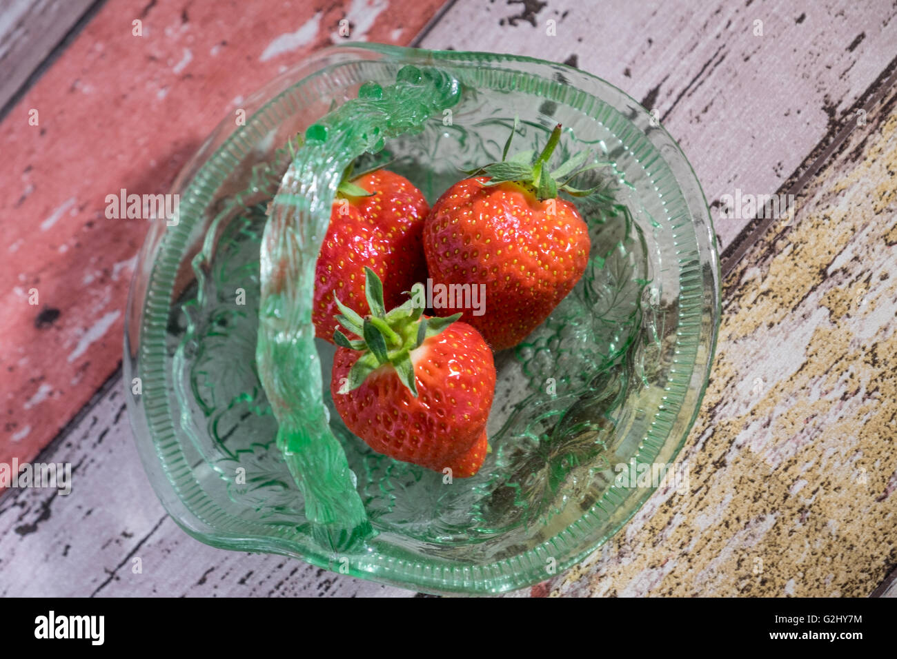 Overhead image of three strawberries in vintage green glass dish on wooden background Stock Photo