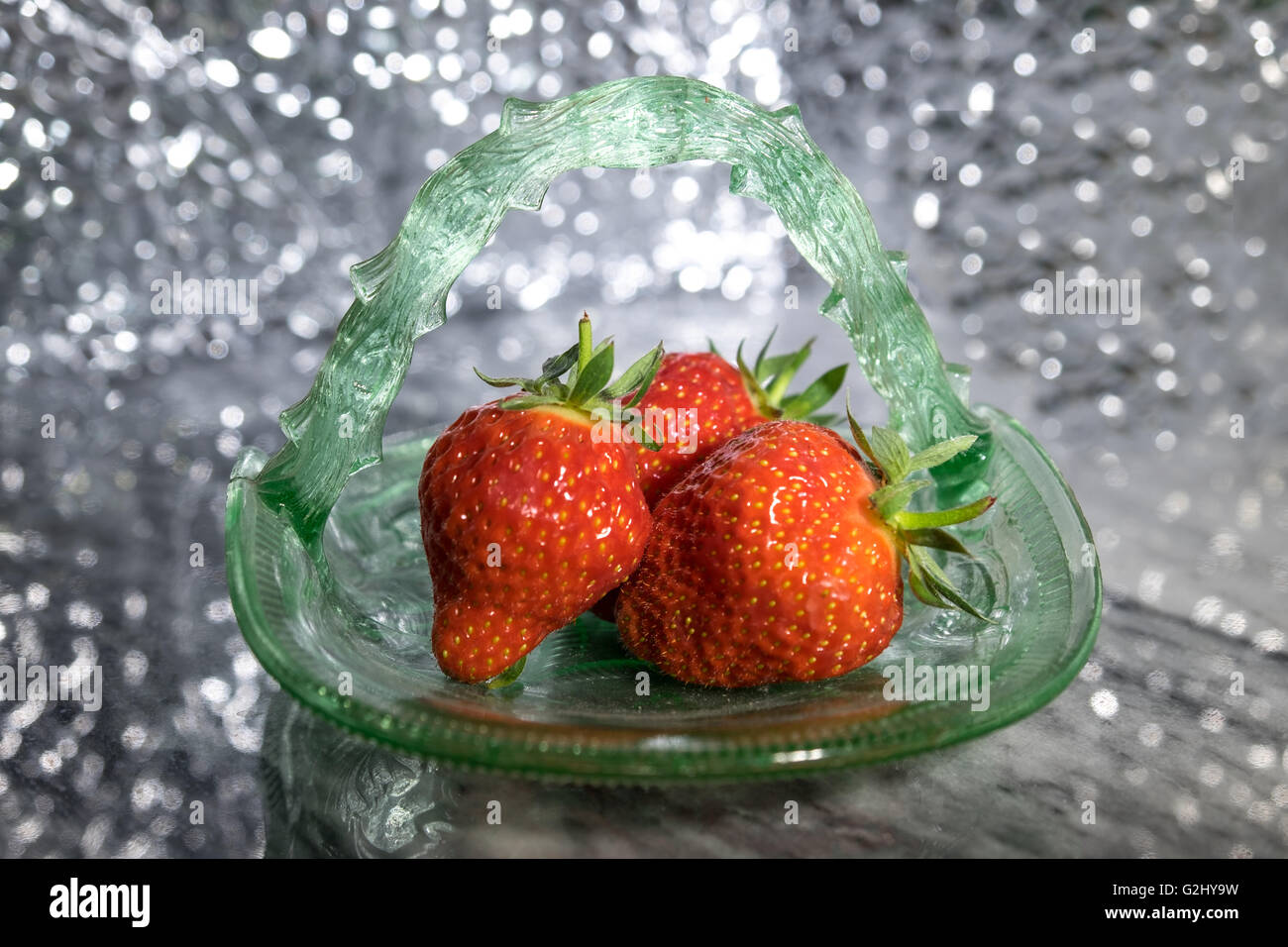 Green glass dish of strawberries against a sparkly background Stock Photo