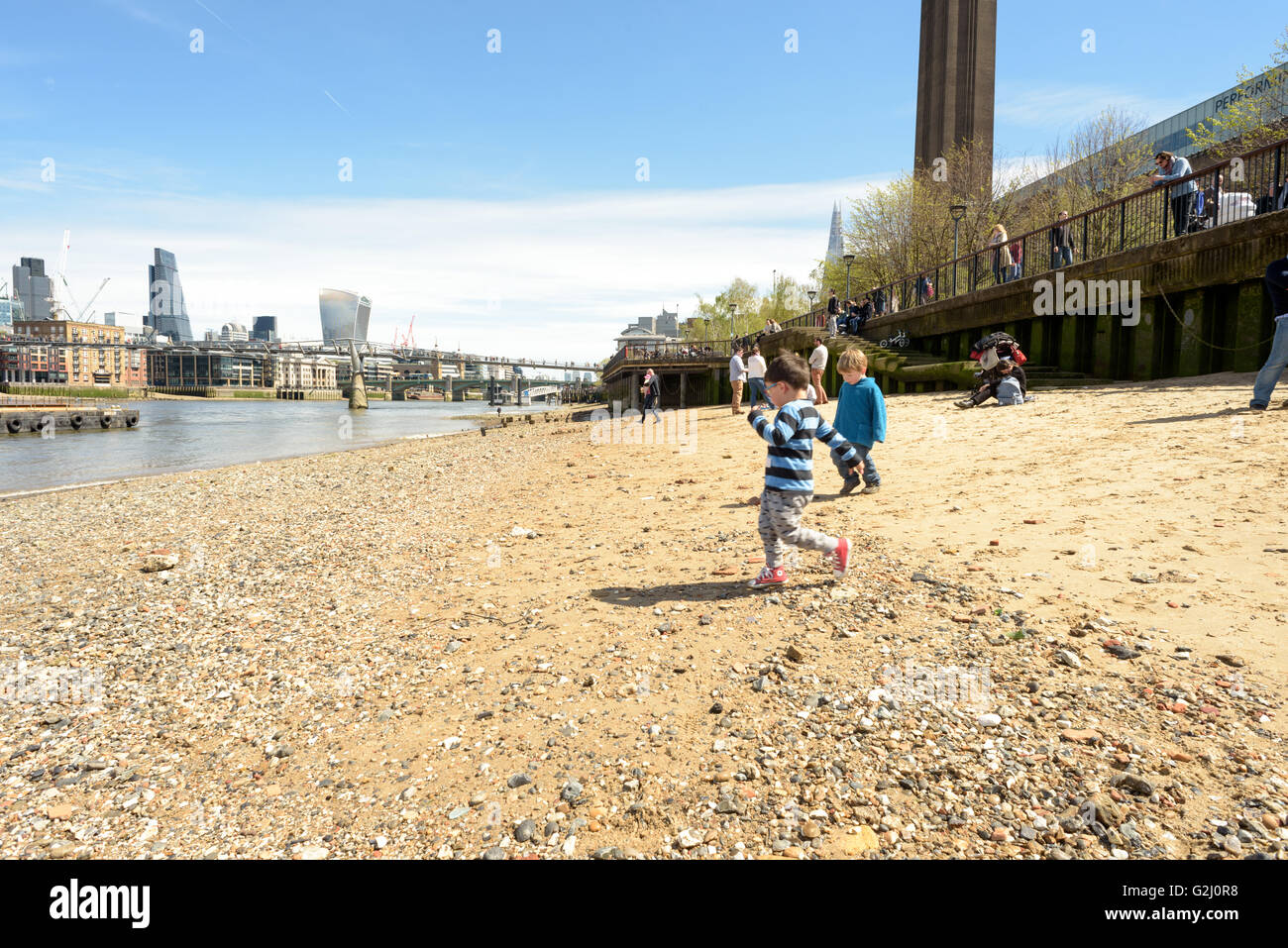 Two children playing on the sandy shores of the River Thames in London at Low Tide in May sunshine 2016 Stock Photo