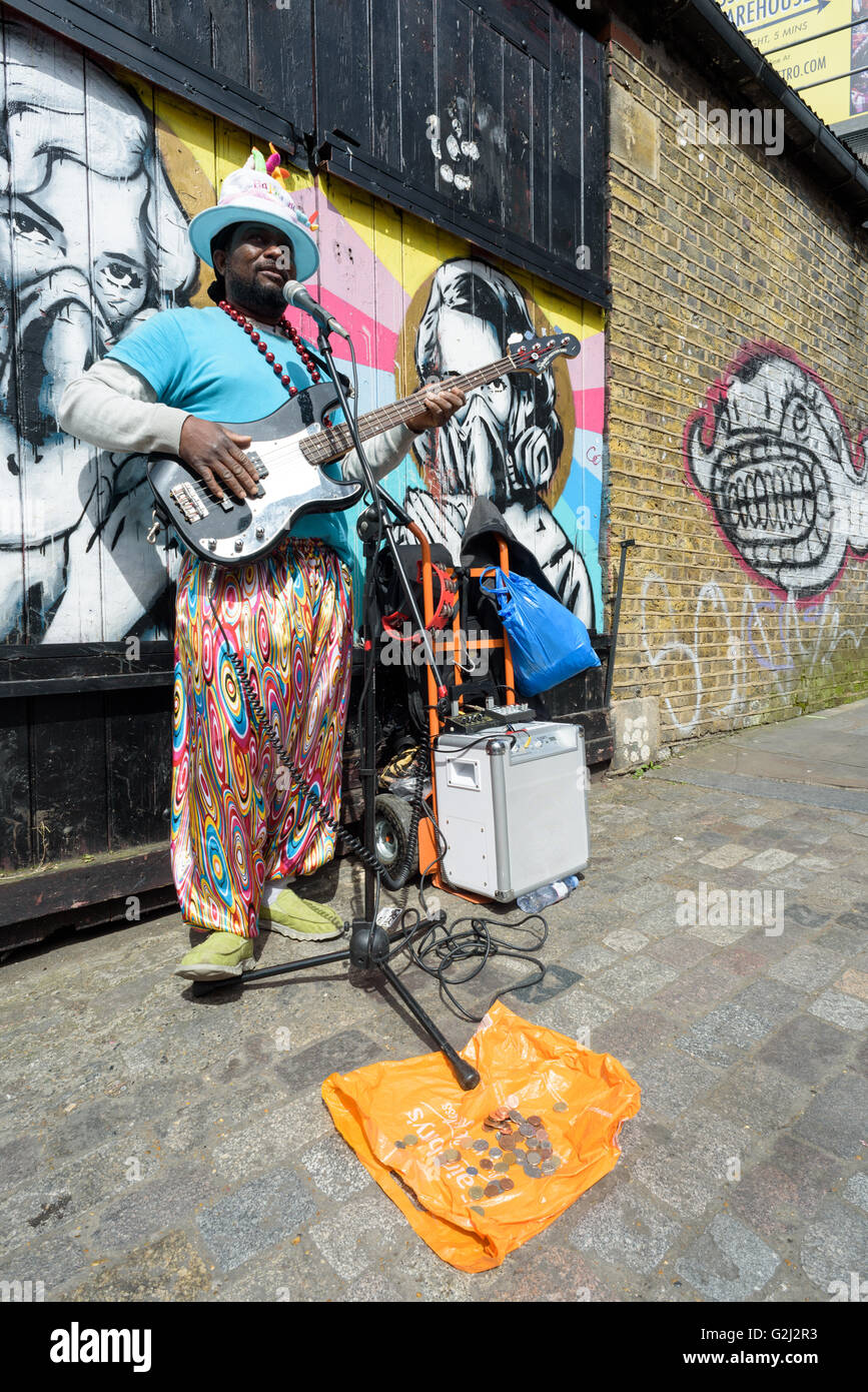 A street busker plays money with an electric guitar for donations on Brick Lane in London during the 1st of May Bank Holiday Stock Photo