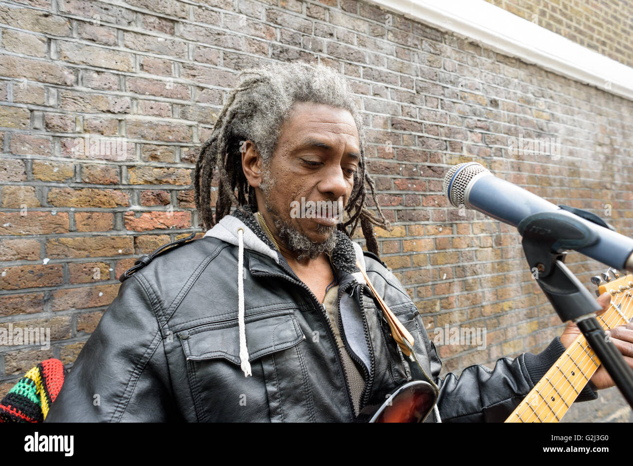 A street busker plays money with an electric guitar for donations on Brick Lane in London during the 1st of May Bank Holiday Stock Photo