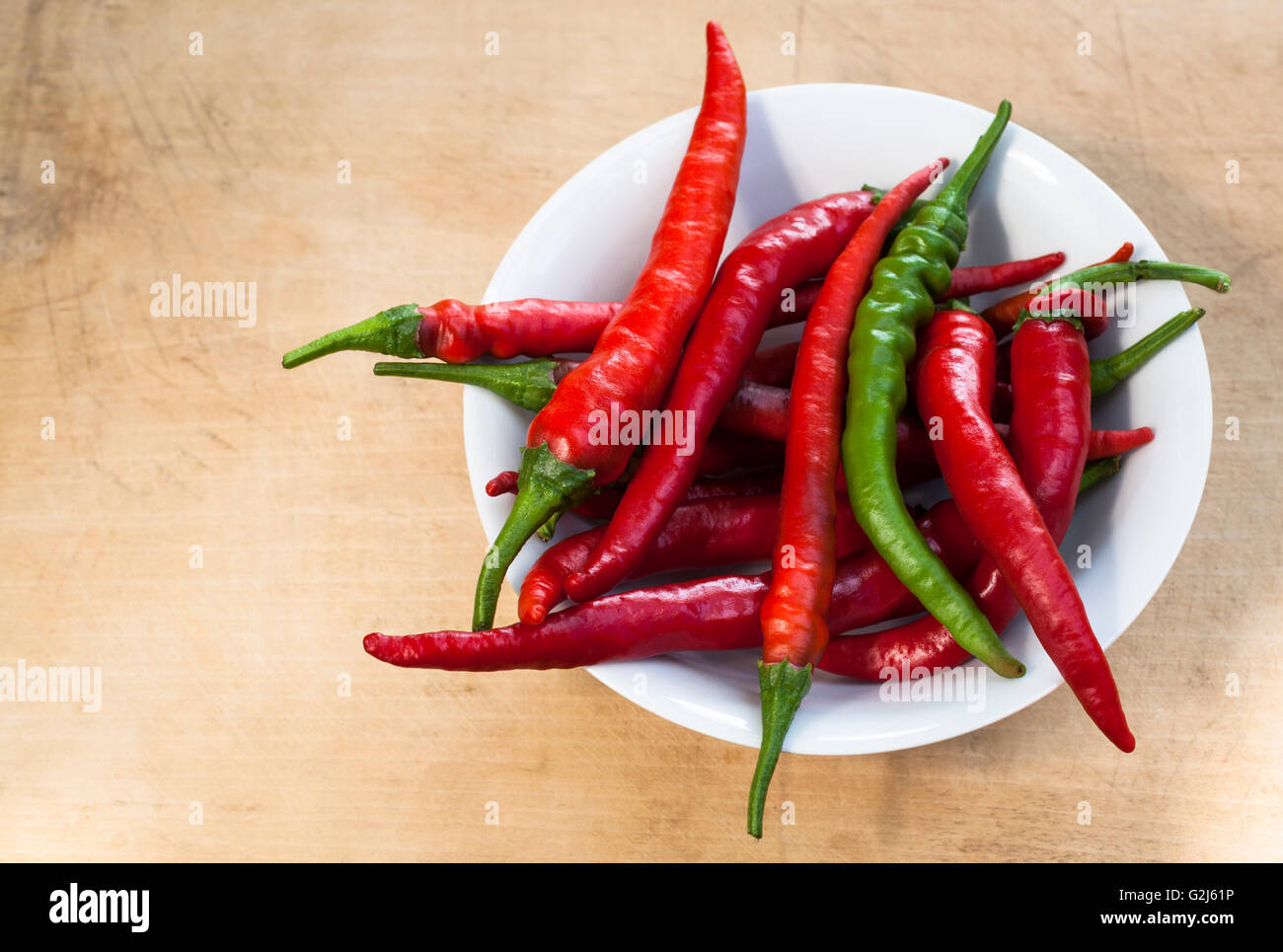 Red chili with one green cilli pepper in a bowl on wood background