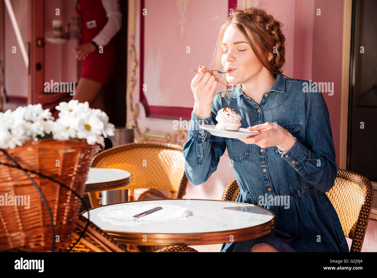 Relaxed pretty young woman sitting and eating cupcake in outdoor cafe Stock Photo