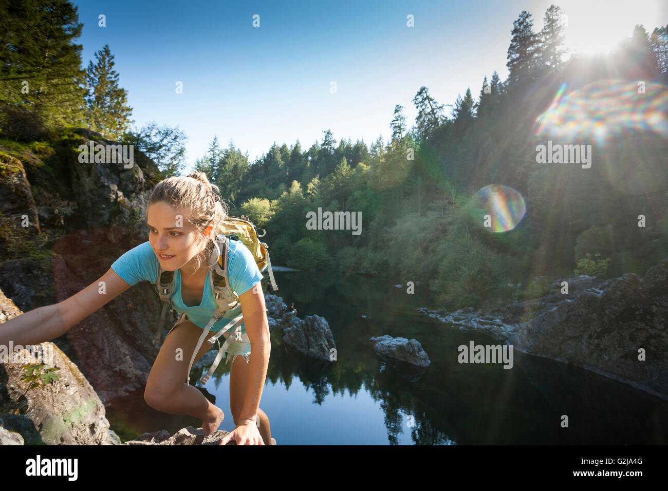 A young woman climbs rocky cliffs at the Sooke Potholes Provincial Park, Vancouver Island, BC, Canada Stock Photo