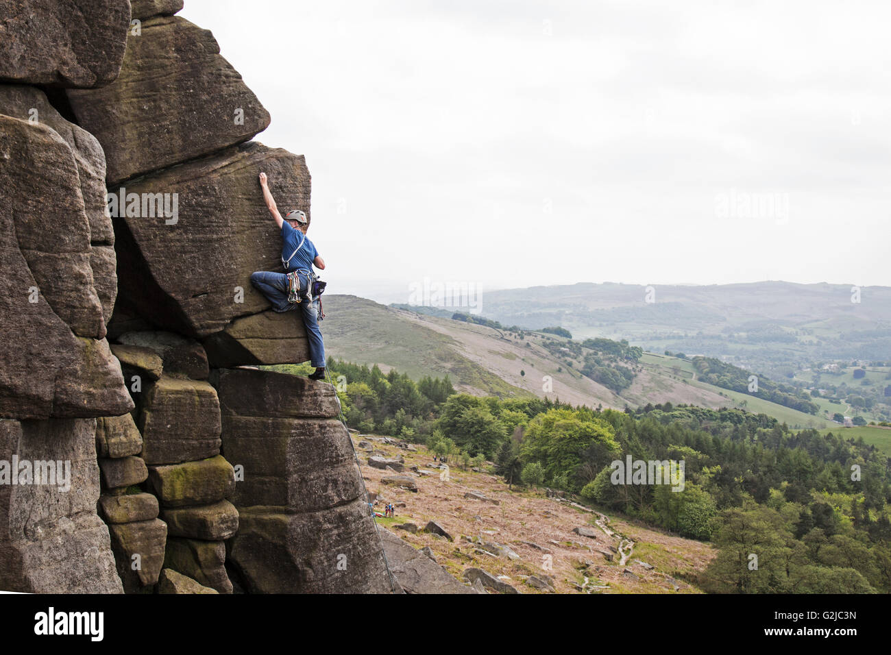 Climber reaching on cliffs of Stanage Plantation in the Peak District, Derbyshire, England. Stock Photo