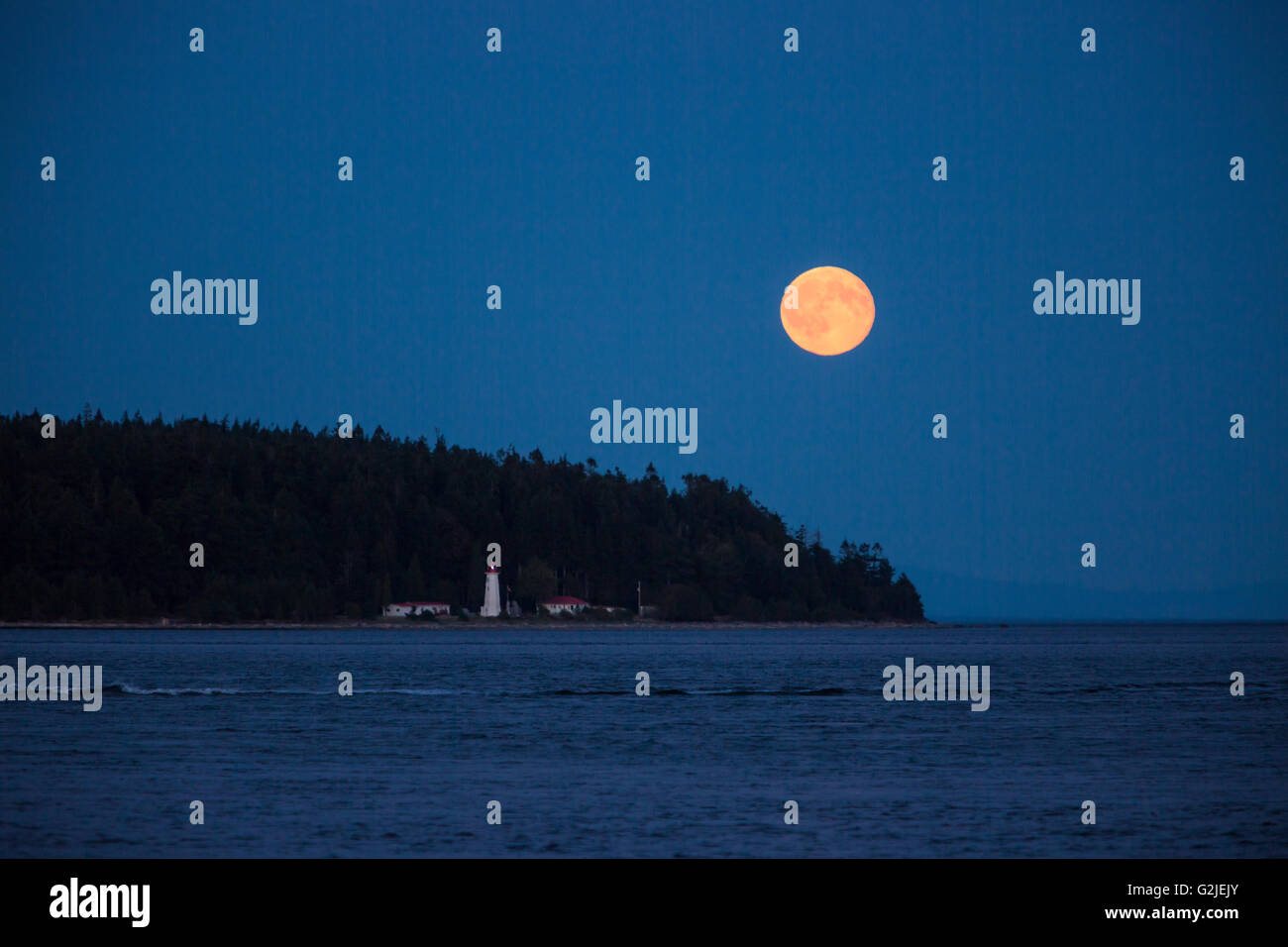 A full moon rises near the Cape Mudge lighthouse on Quadra Island.  Campbell River, Vancouver Island, British Columbia, Canada Stock Photo