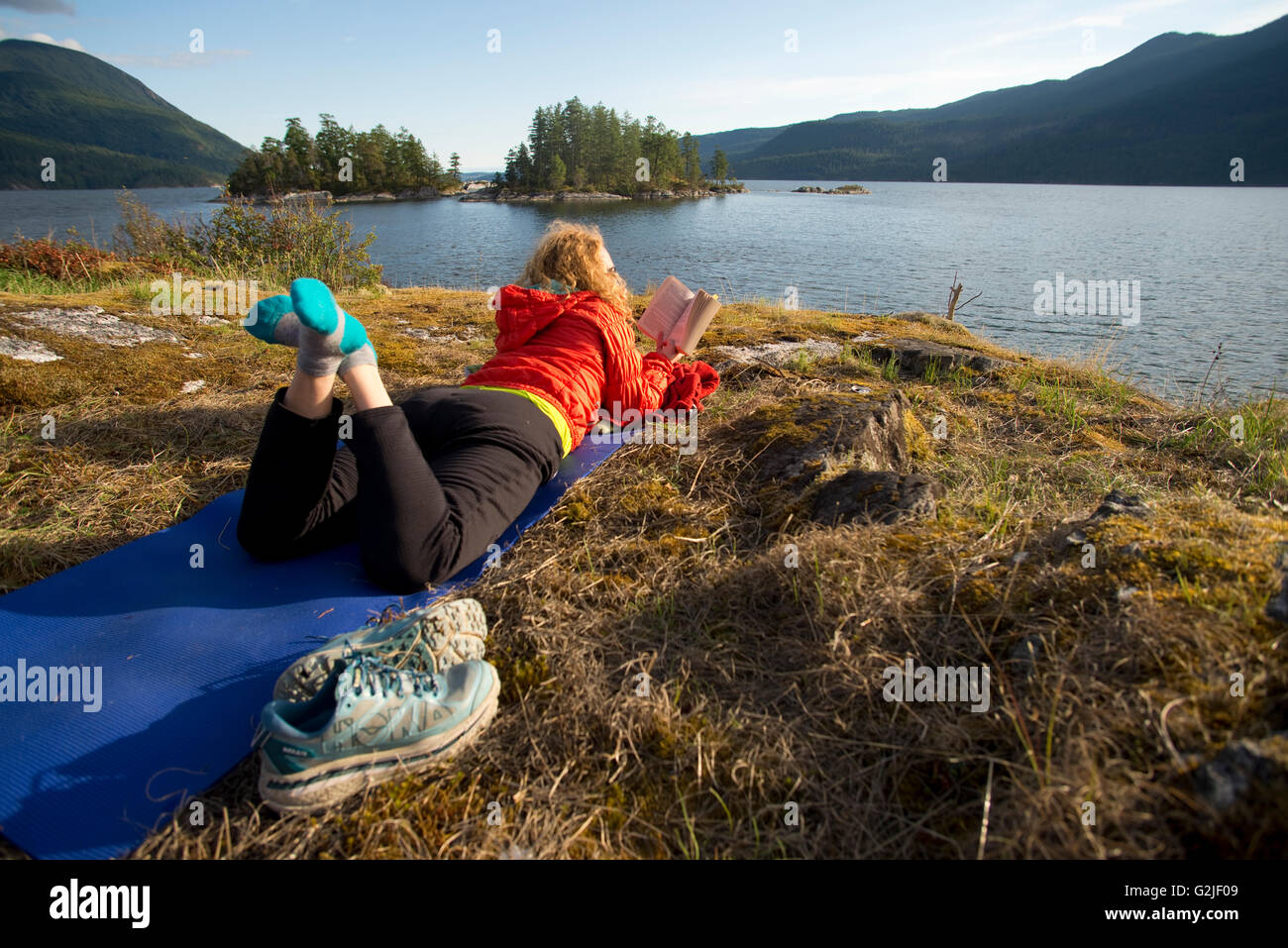 Woman reading book on yoga mat while camping at Kunechin Point. Sechelt Inlet. Sechelt, British Columbia. Canada Stock Photo