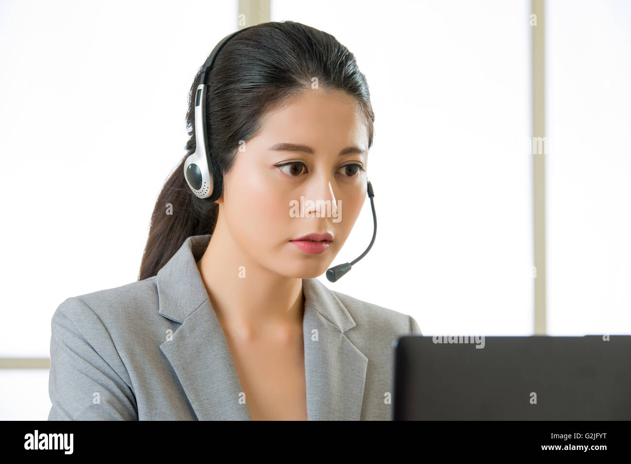 Smiling Asian woman with a headphone and working on laptop in office ...
