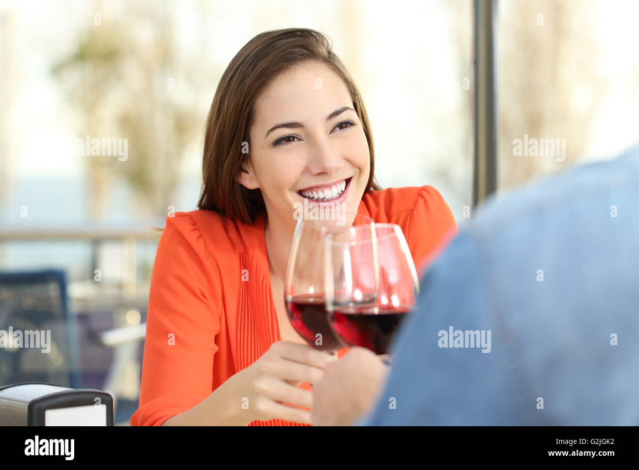 Happy woman toasting with red wine with her partner or friend during a date in a coffee shop interior with a window Stock Photo