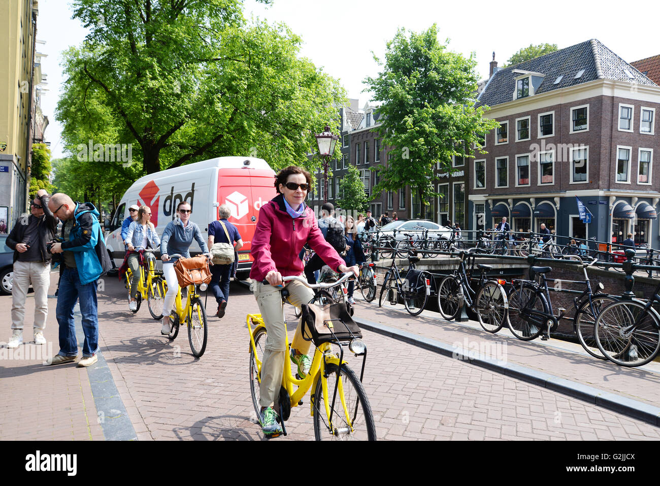 Cyclists in Bike City Amsterdam ride along canal road on bright yellow