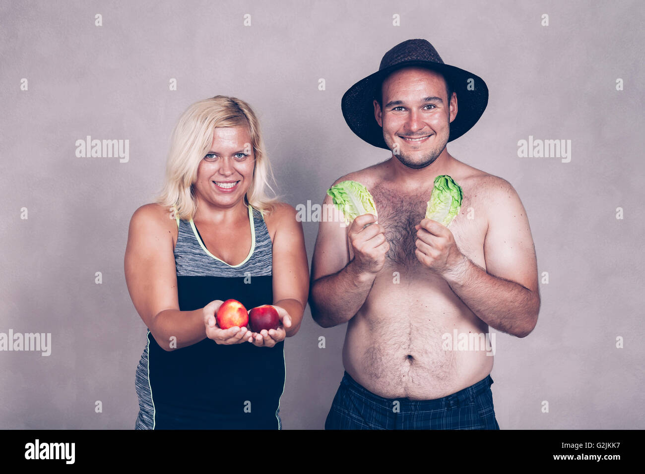 Funny young corpulent couple holding lettuce and nectarine. Stock Photo