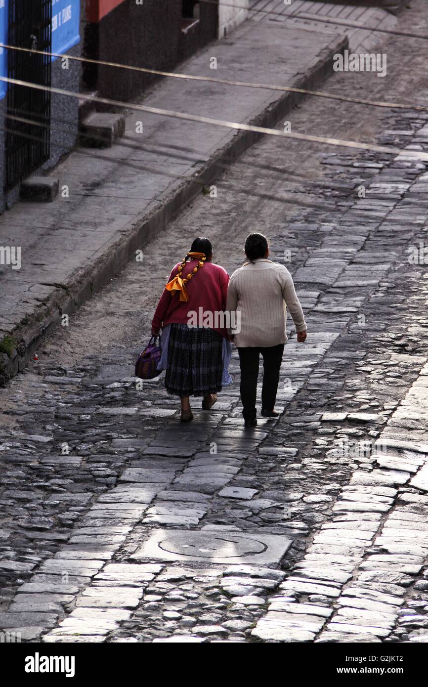 A Mayan Guatemalan mother and grandmother walk down a wet reflective cobblestone street in Quetzaltenango Stock Photo