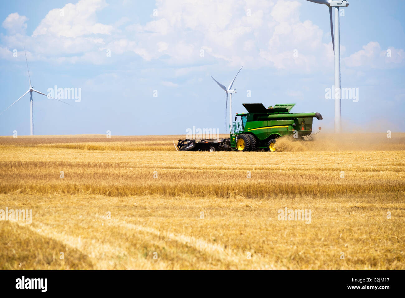 A John Deere combine harvests wheat in Oklahoma, USA.Wind farm in background. Stock Photo