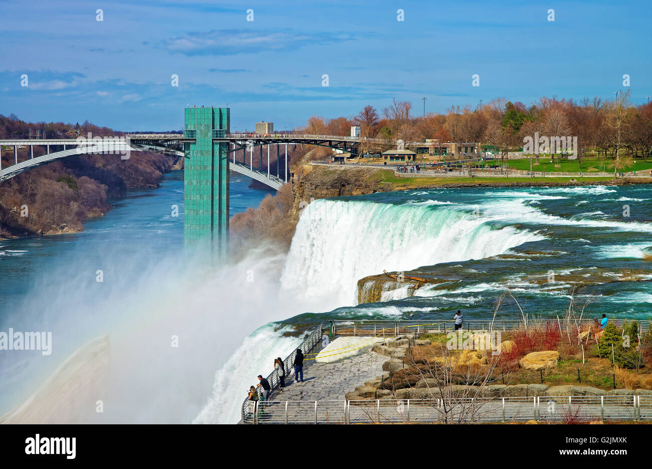 Rainbow in Niagara Falls and Rainbow Bridge over Niagara River Gorge from American side. It is an arch bridge between the United States of America and Canada. Tourists in the Park Stock Photo