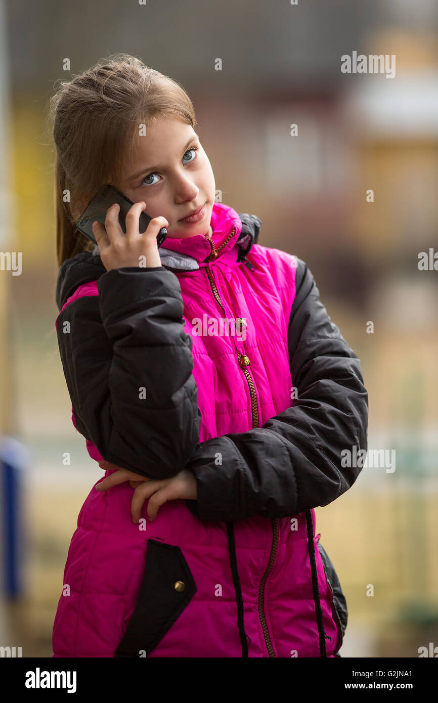 Little girl standing on the street talking on a cell phone. Stock Photo