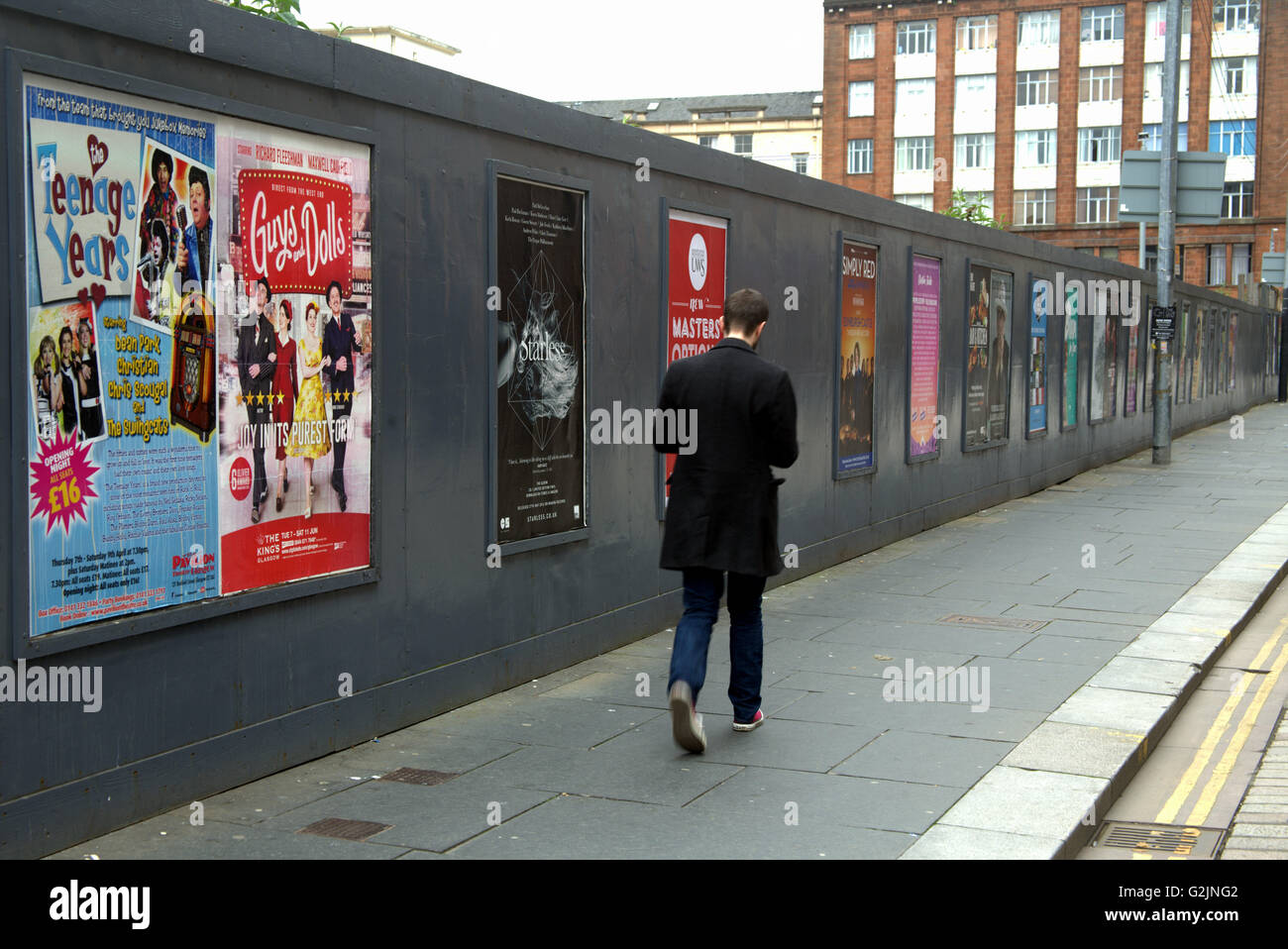 young man walks along pavement in front of entertainment posters, Glasgow, Scotland, UK. Stock Photo