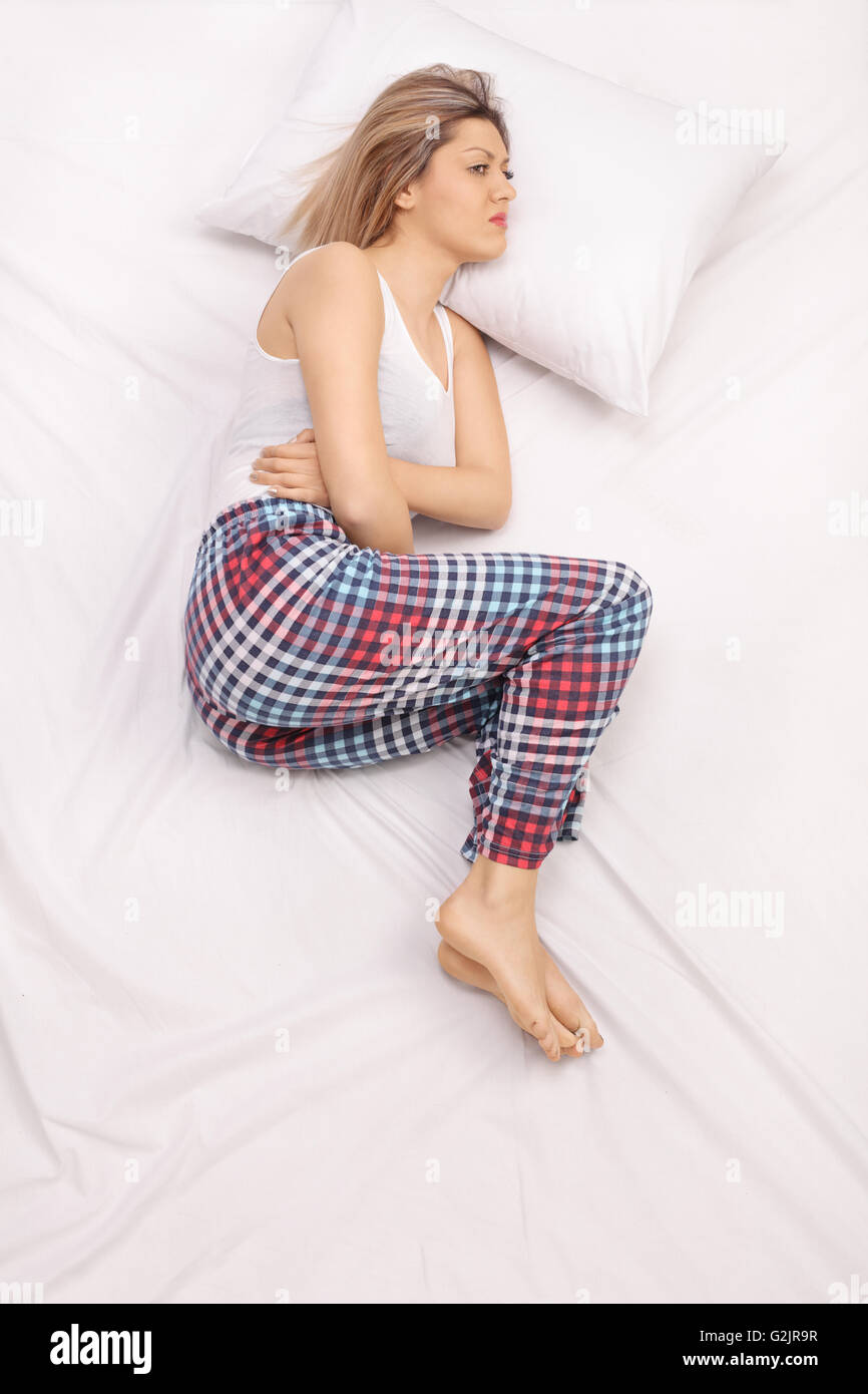 Vertical shot of a displeased woman feeling a stomach ache and laying on a bed Stock Photo