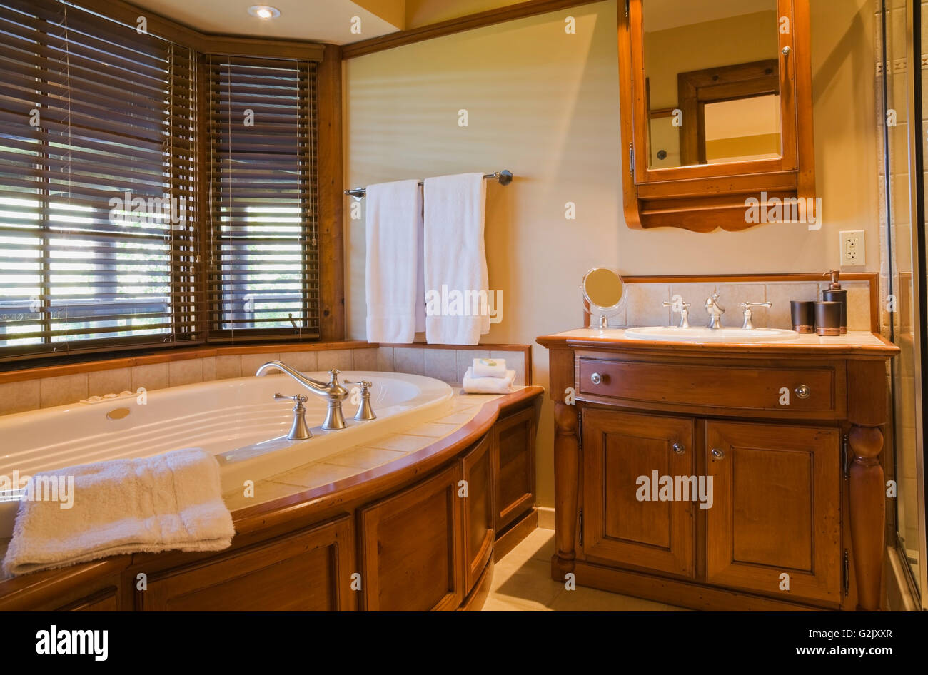 Guest bedroom ensuite oval Jacuzzi wooden vanity in basement inside a luxurious cottage style log home Quebec Canada This image Stock Photo