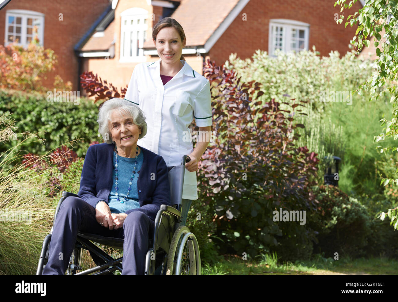 Portrait Of Carer Pushing Senior Woman In Wheelchair Stock Photo