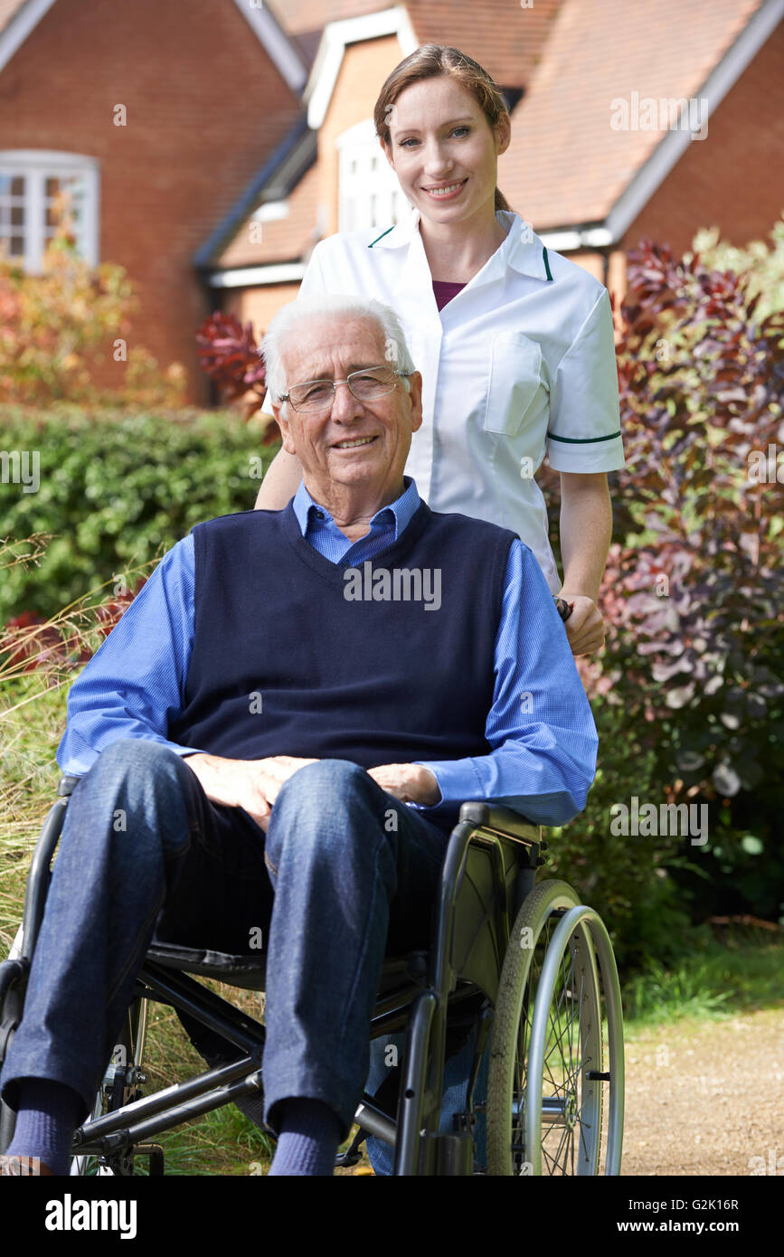 Portrait Of Carer Pushing Senior Man In Wheelchair Stock Photo