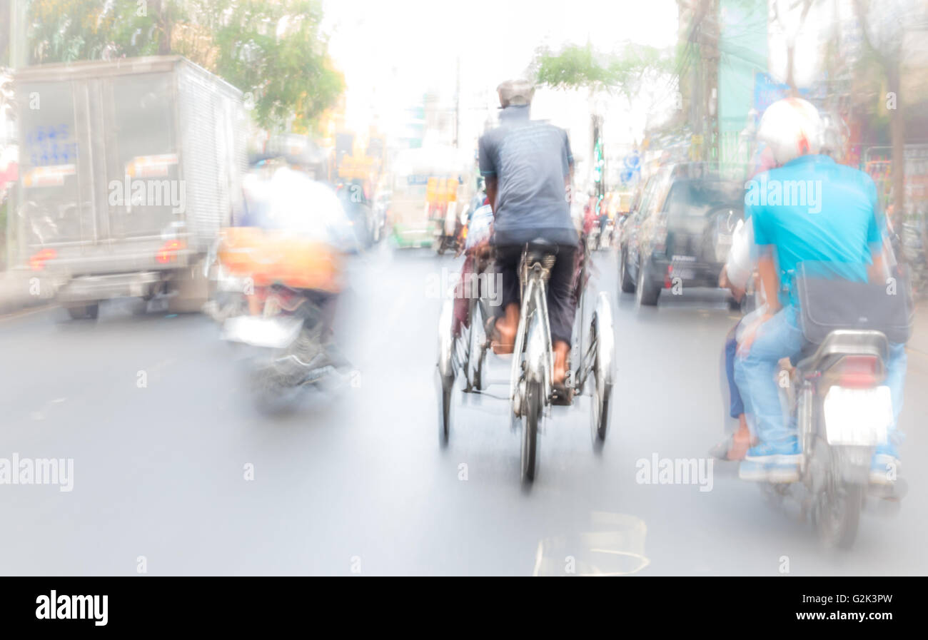 Traffic, cars, rickshaw: Artistic capture of a rickshaw rider travelling down a busy road with a tourist in Ho Chi Minh City, Vietnam, Asia Stock Photo