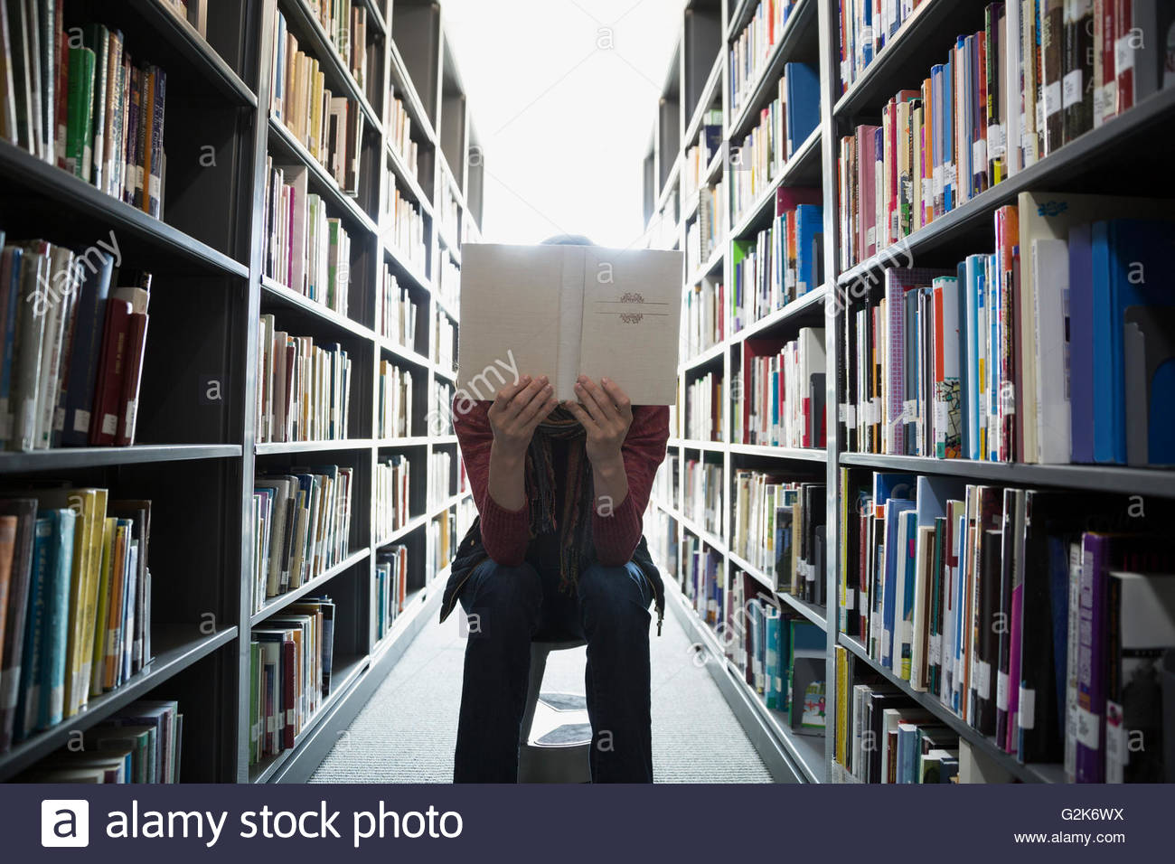 Adult education student reading between library bookshelves Stock Photo
