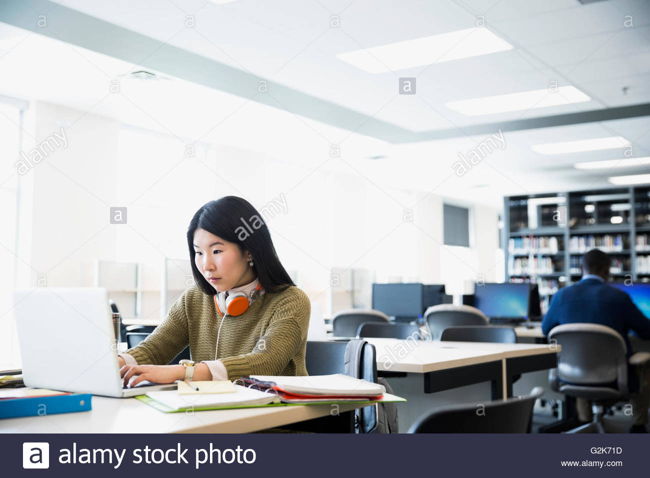 College student with headphones researching at laptop in library Stock Photo