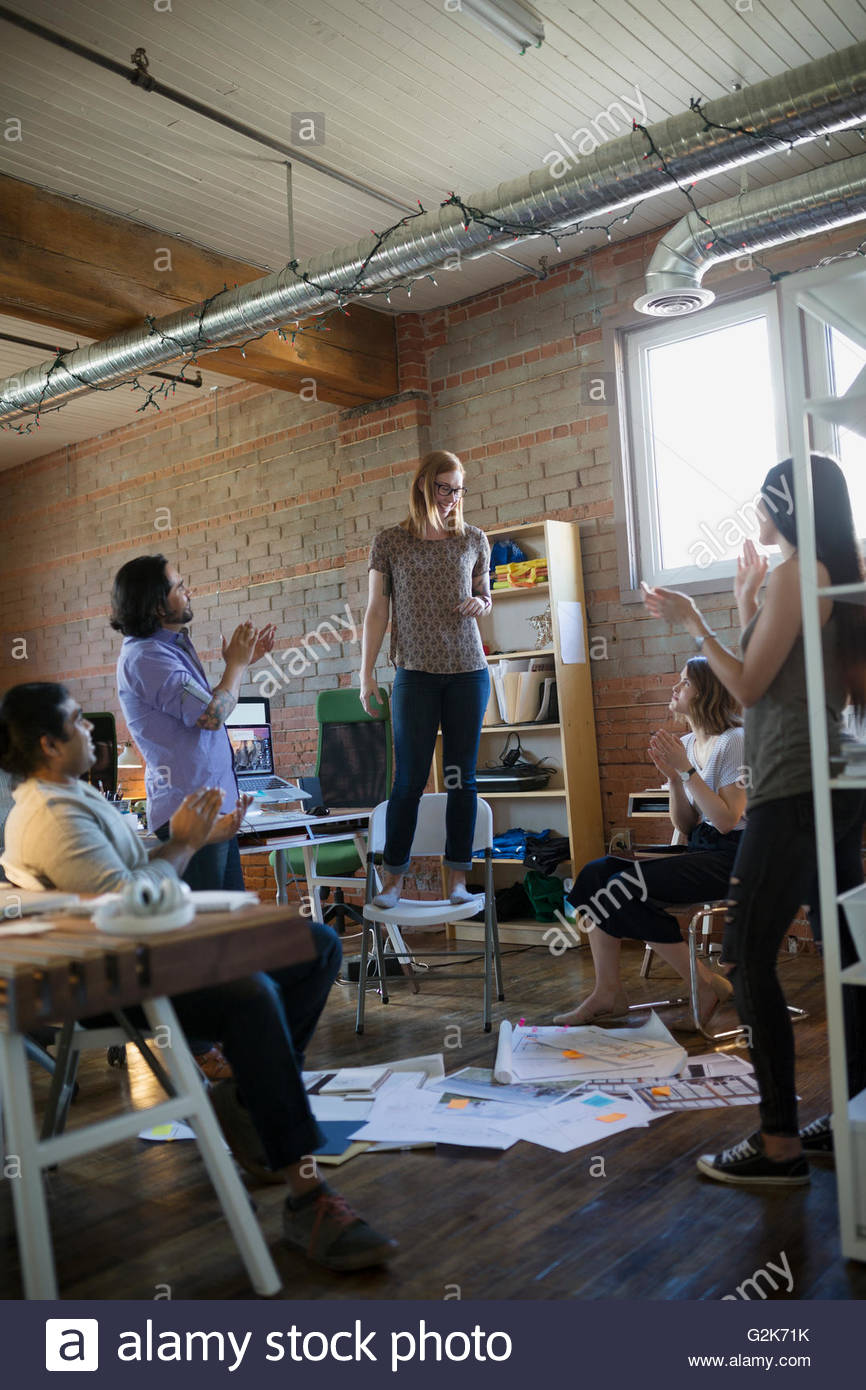 Coworkers clapping for designer standing on chair in office Stock Photo