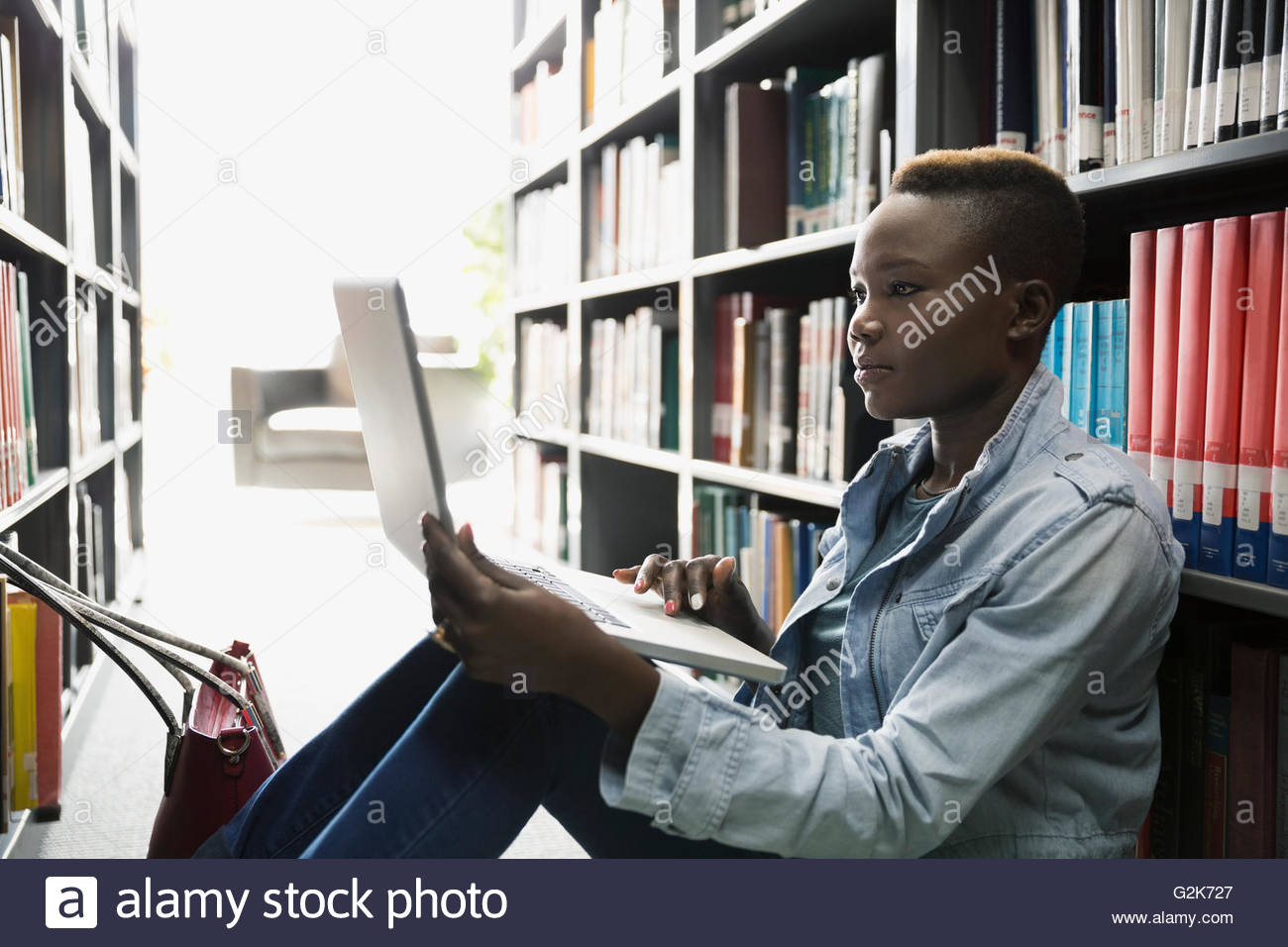College student using laptop between library bookshelves Stock Photo Alamy