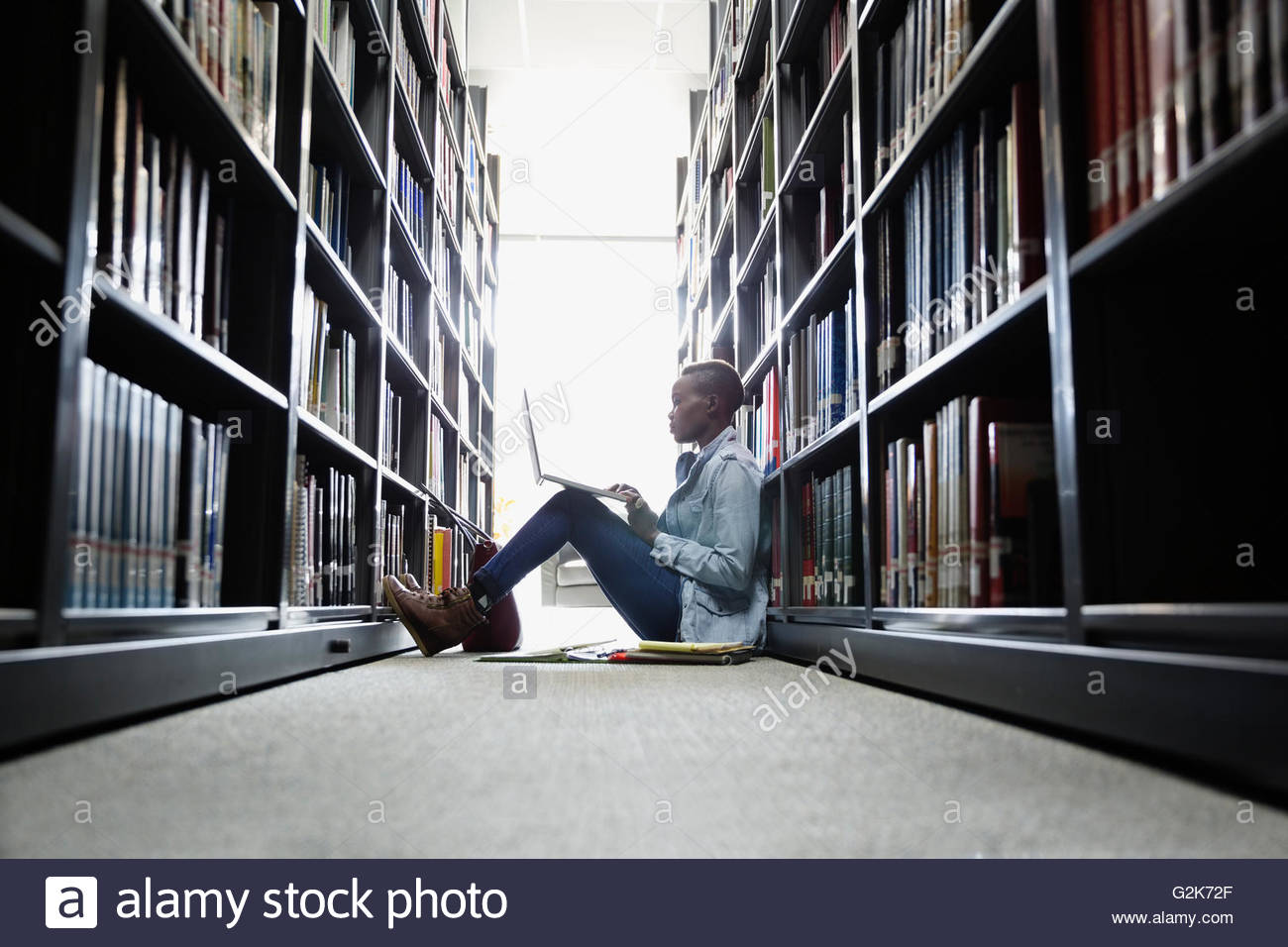 College student using laptop between library bookshelves Stock Photo Alamy