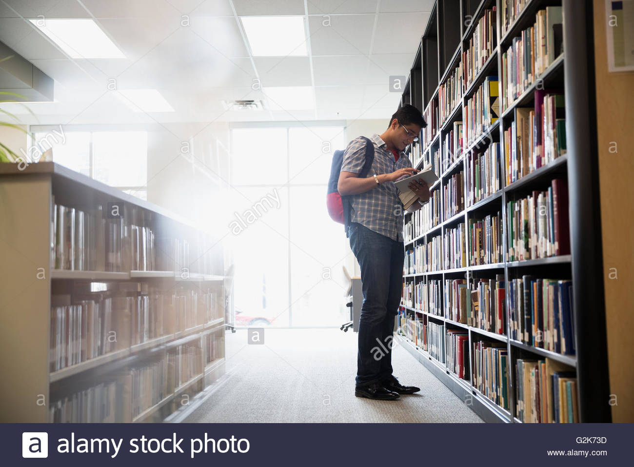 College student reading book at bookshelf in library Stock Photo Alamy