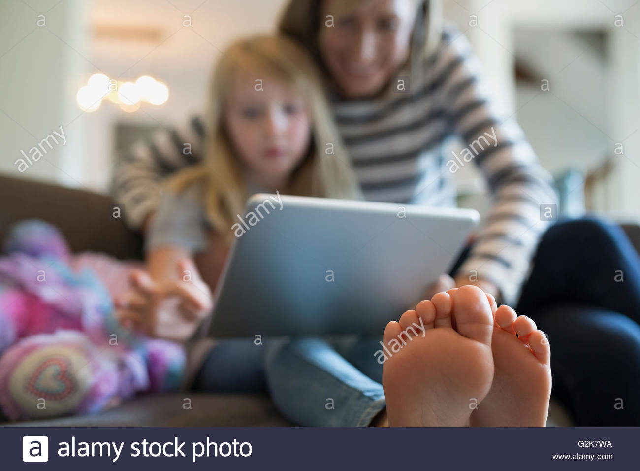 Mother and barefoot daughter using digital tablet on sofa Stock Photo