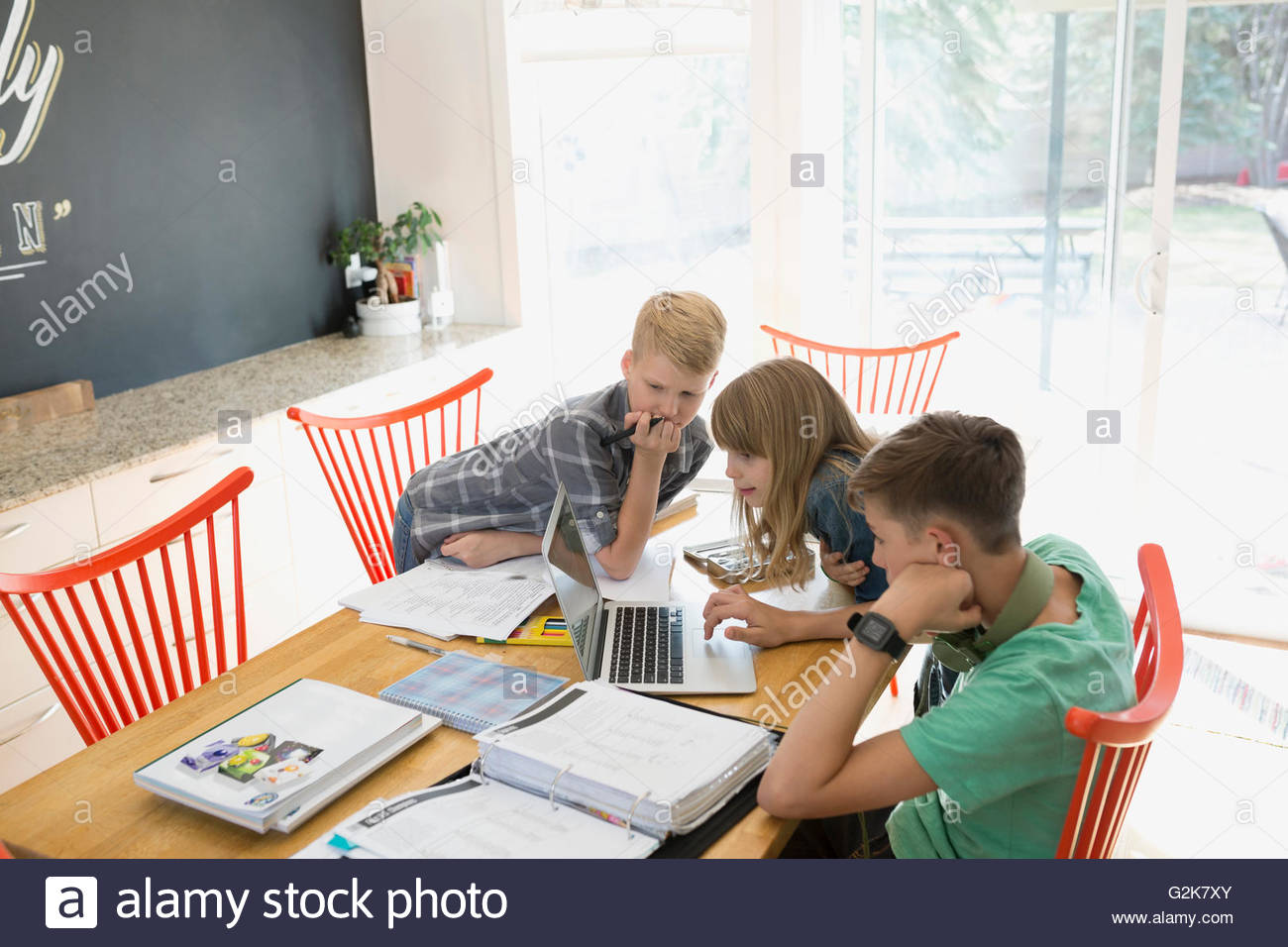 Brothers and sister doing homework at laptop at dining table Stock Photo