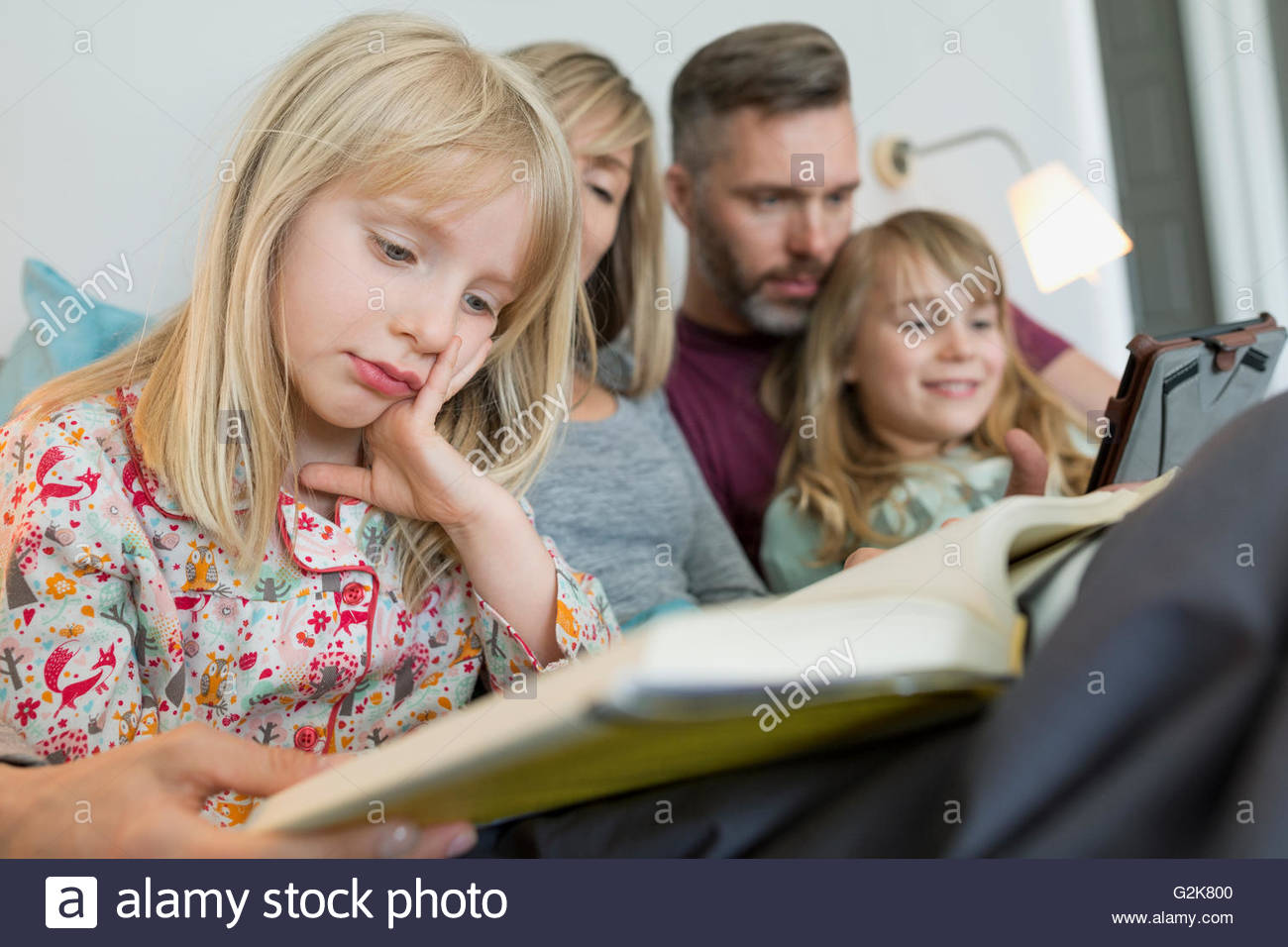 Family relaxing reading book and using digital tablet in bed Stock Photo